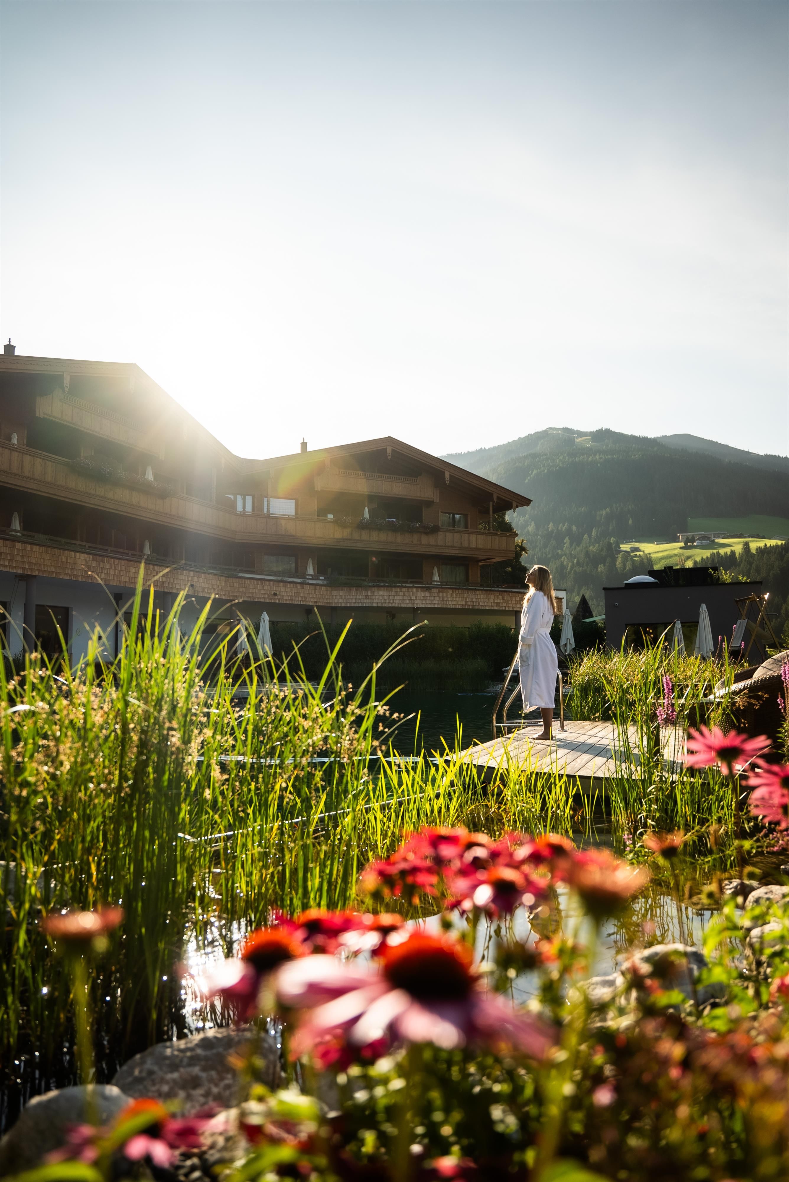 A beautiful viewpoint with flowers and green vegetation. In the background, buildings and the sunset are visible.