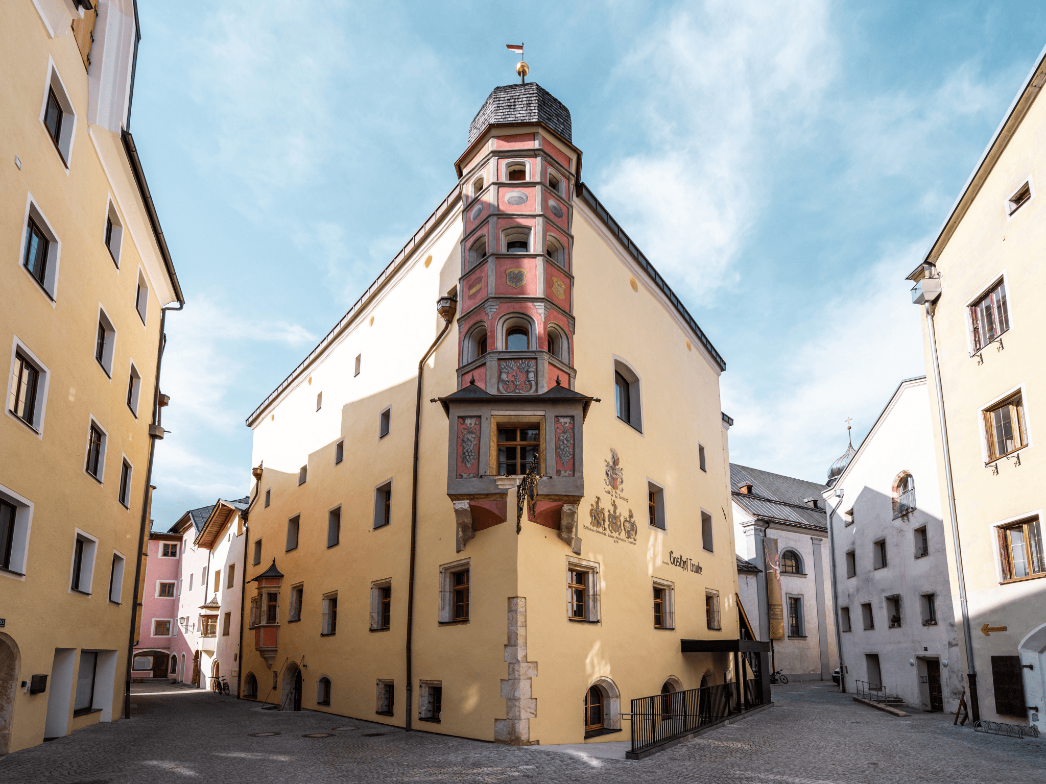 A historic building with colorful frescoes and a distinctive façade. It stands between narrow, bright streets in a charming town.