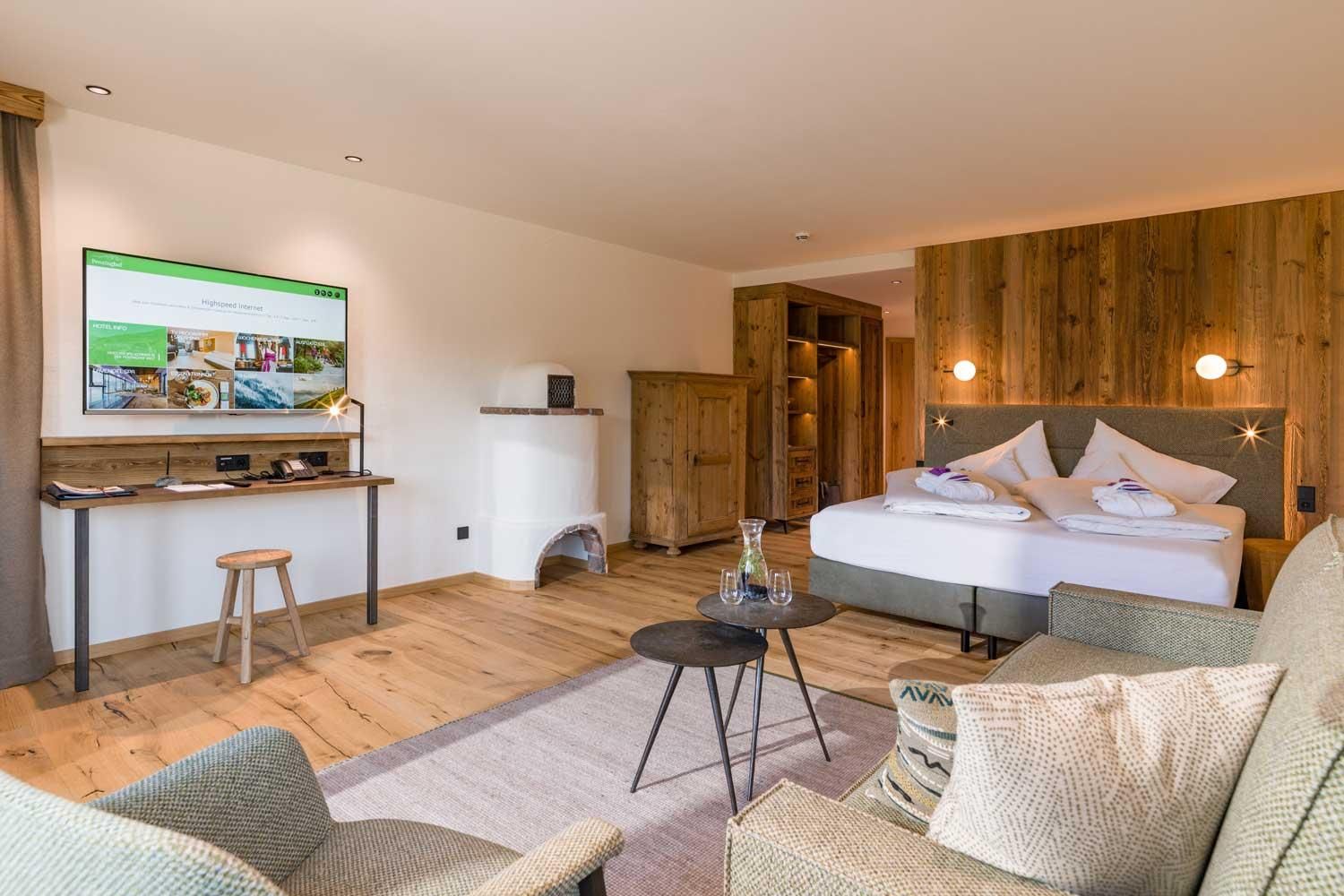 A modern bedroom with wood paneling and cozy furniture. There is a double bed, a table, and a comfortable seating area.