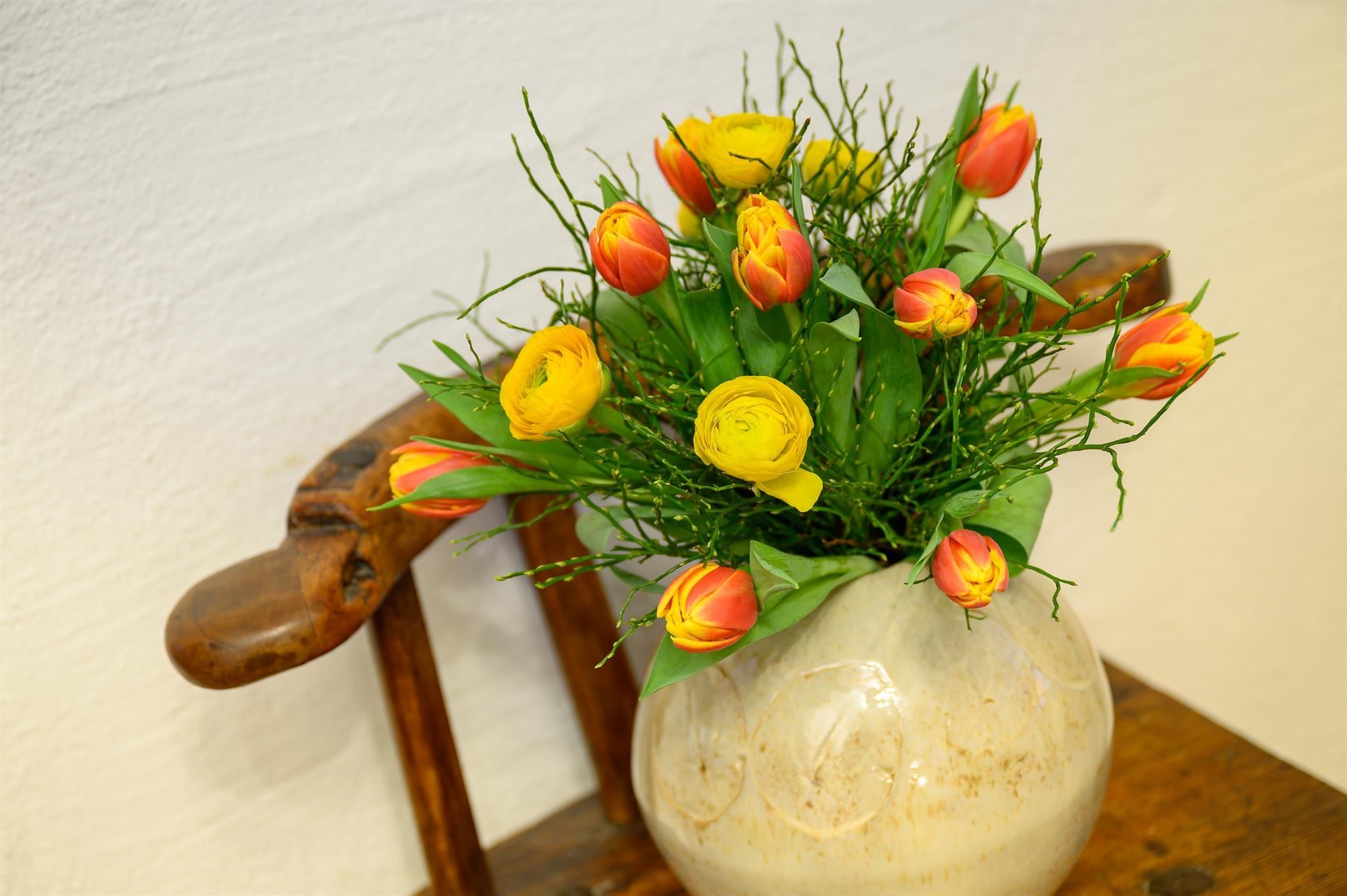 A beautiful bouquet of red and yellow tulips in a decorative vase. The bouquet is on a wooden chair.