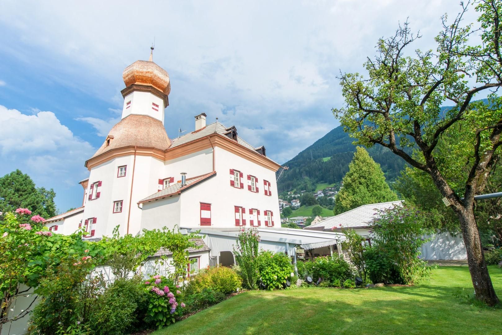 A charming building with a distinctive dome in a green setting. In the background, gentle hills and a blue sky can be seen.
