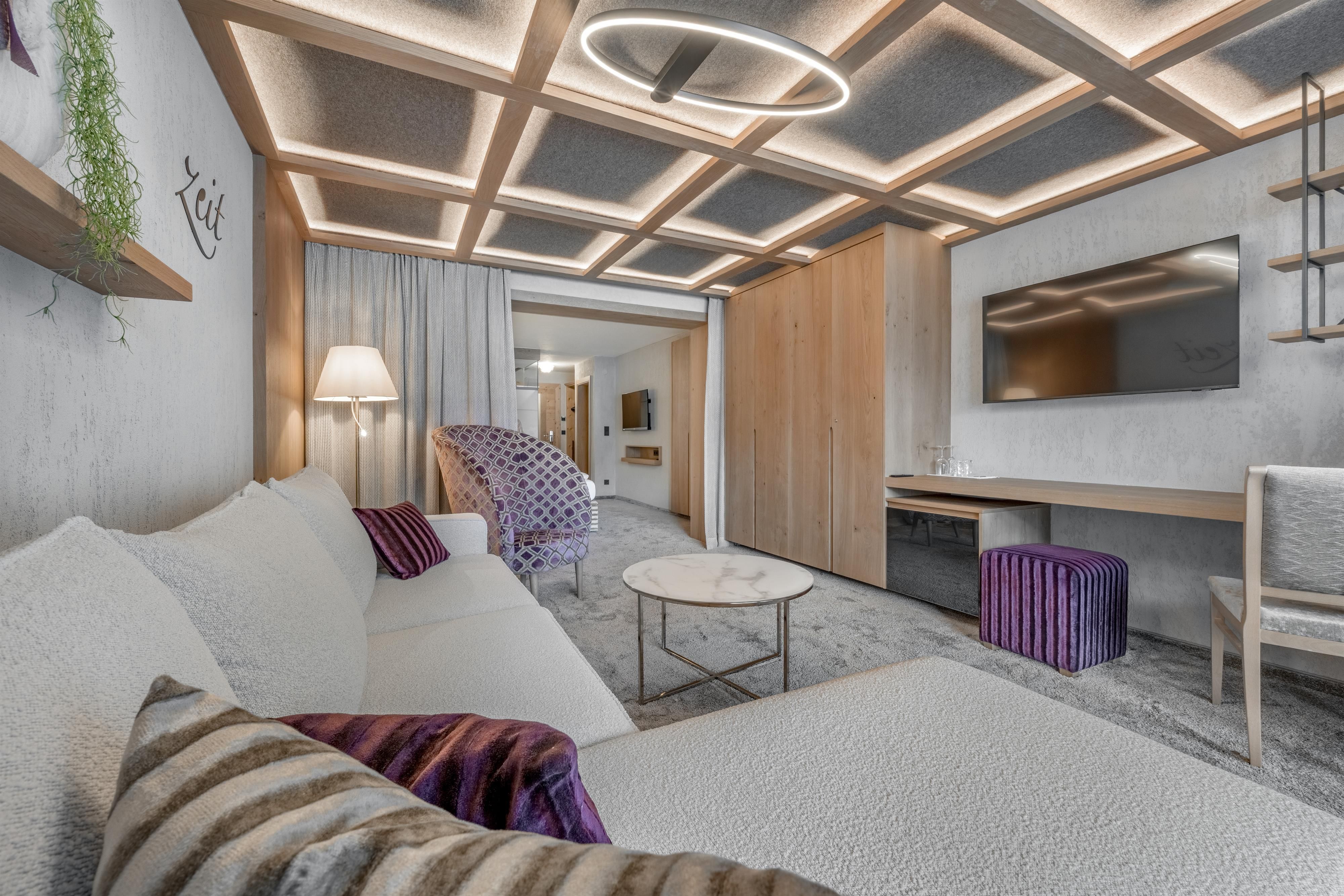 A modern living environment with a white sofa, a coffee table, and a large television. The renovation provides warm light and a cozy atmosphere.