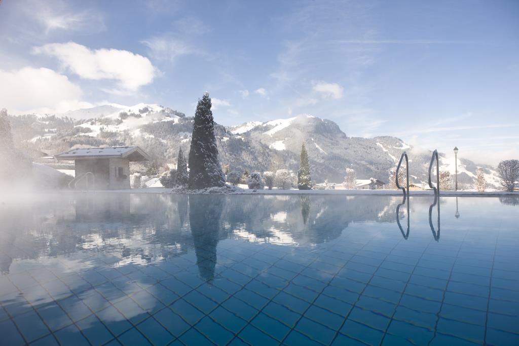 A beautiful outdoor pool in a winter landscape. The mountains and the clear sky are reflected in the water.
