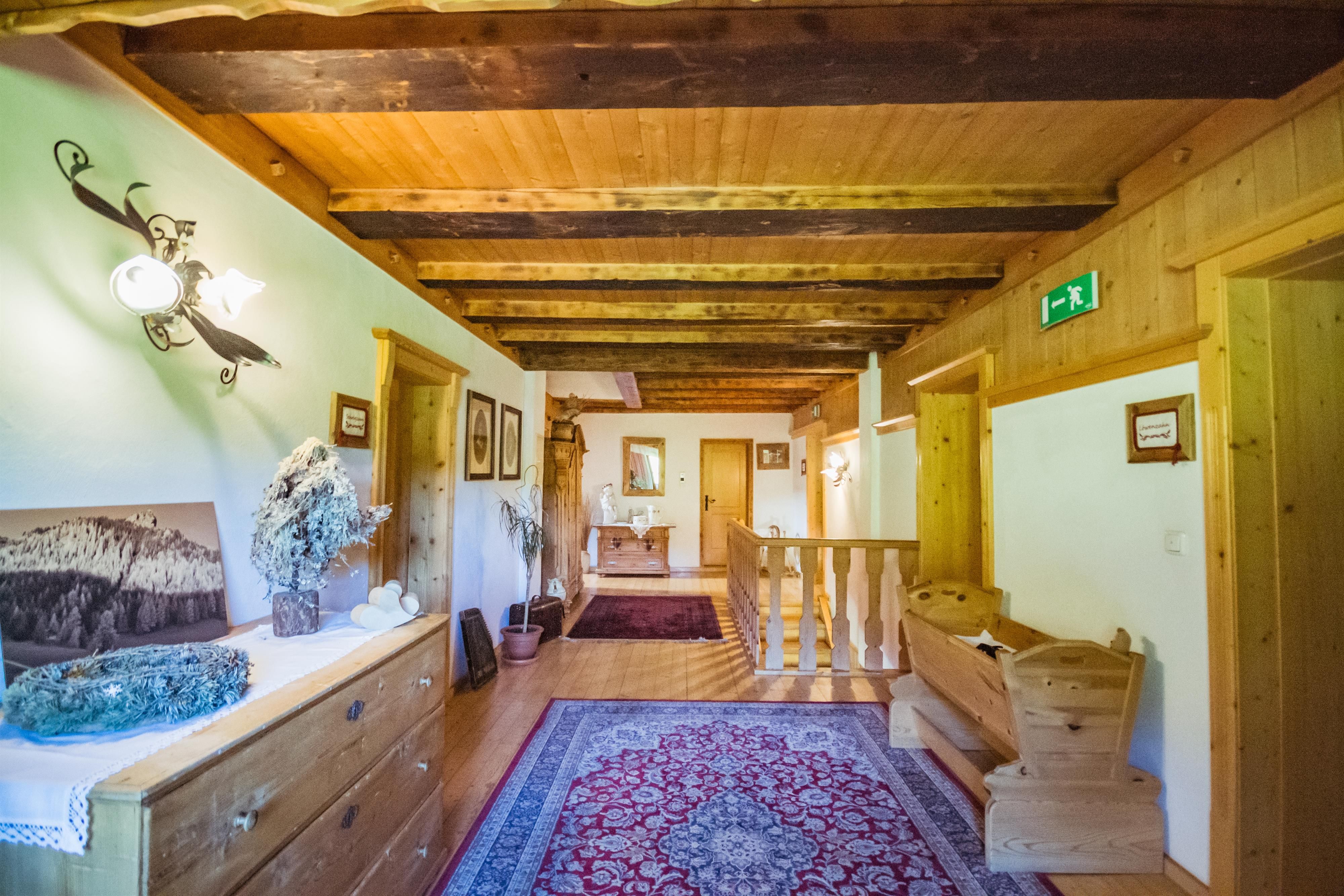 A cozy hallway with a wooden ceiling and warm light. Pictures hang on the walls, and a carpet gives the room an inviting atmosphere.