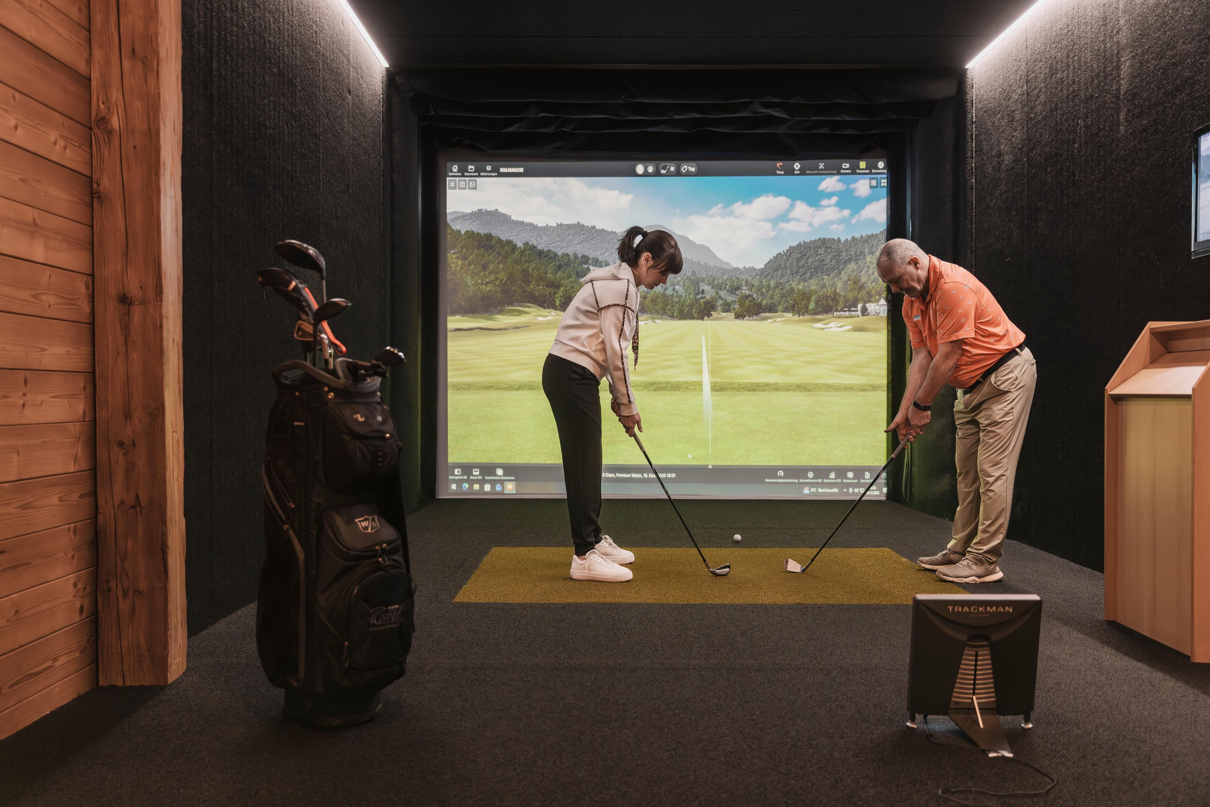 An indoor golf facility with a simulator. A man and a woman are practicing golf on the virtual platform.