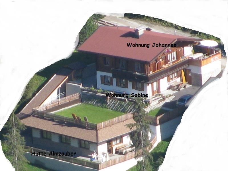 An aerial shot of two holiday apartments in the mountains. The buildings have balconies and are surrounded by green spaces.