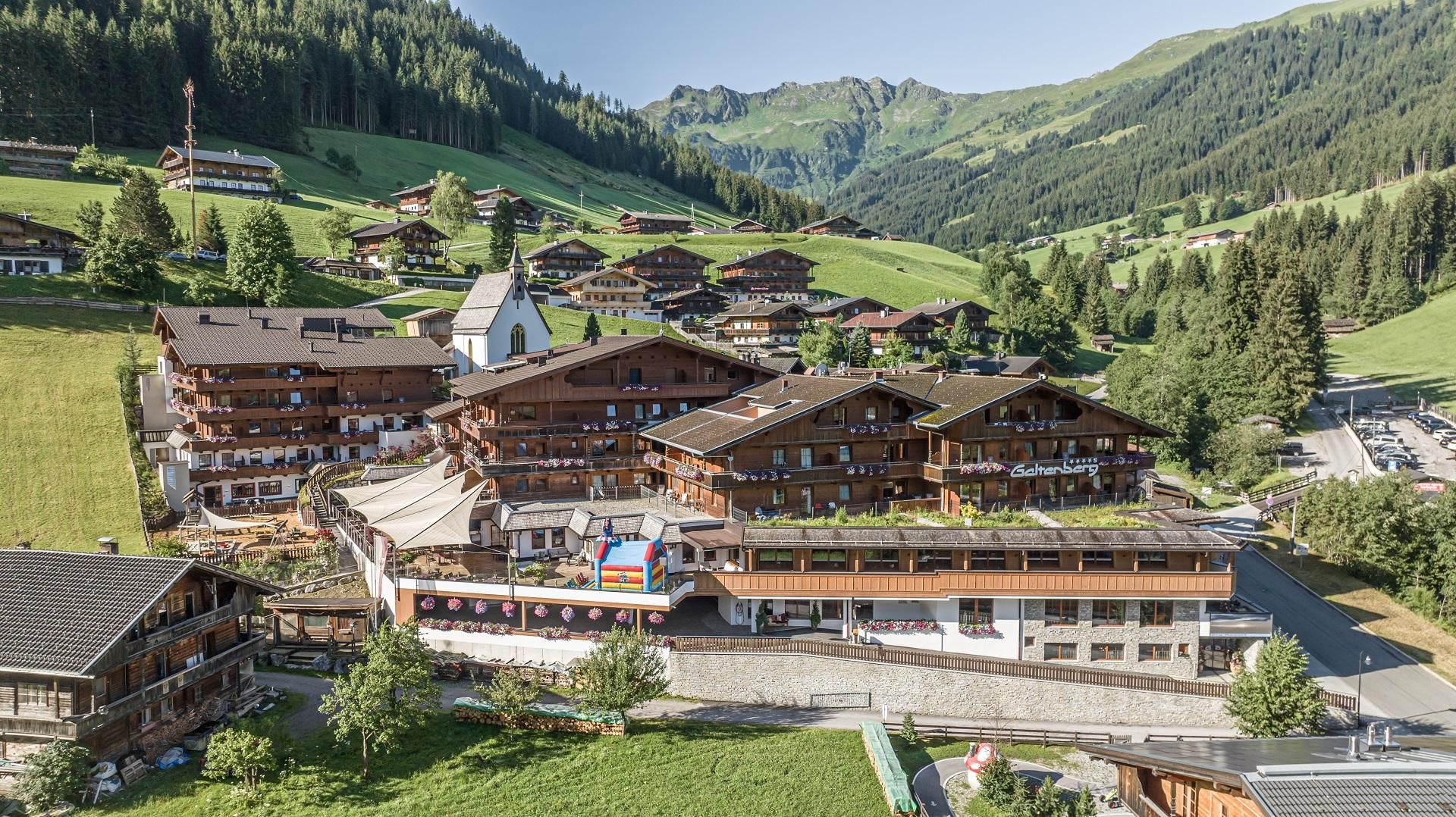 A picturesque mountain landscape with traditional wooden houses and green meadows. In the background, gentle hills and forests can be seen.