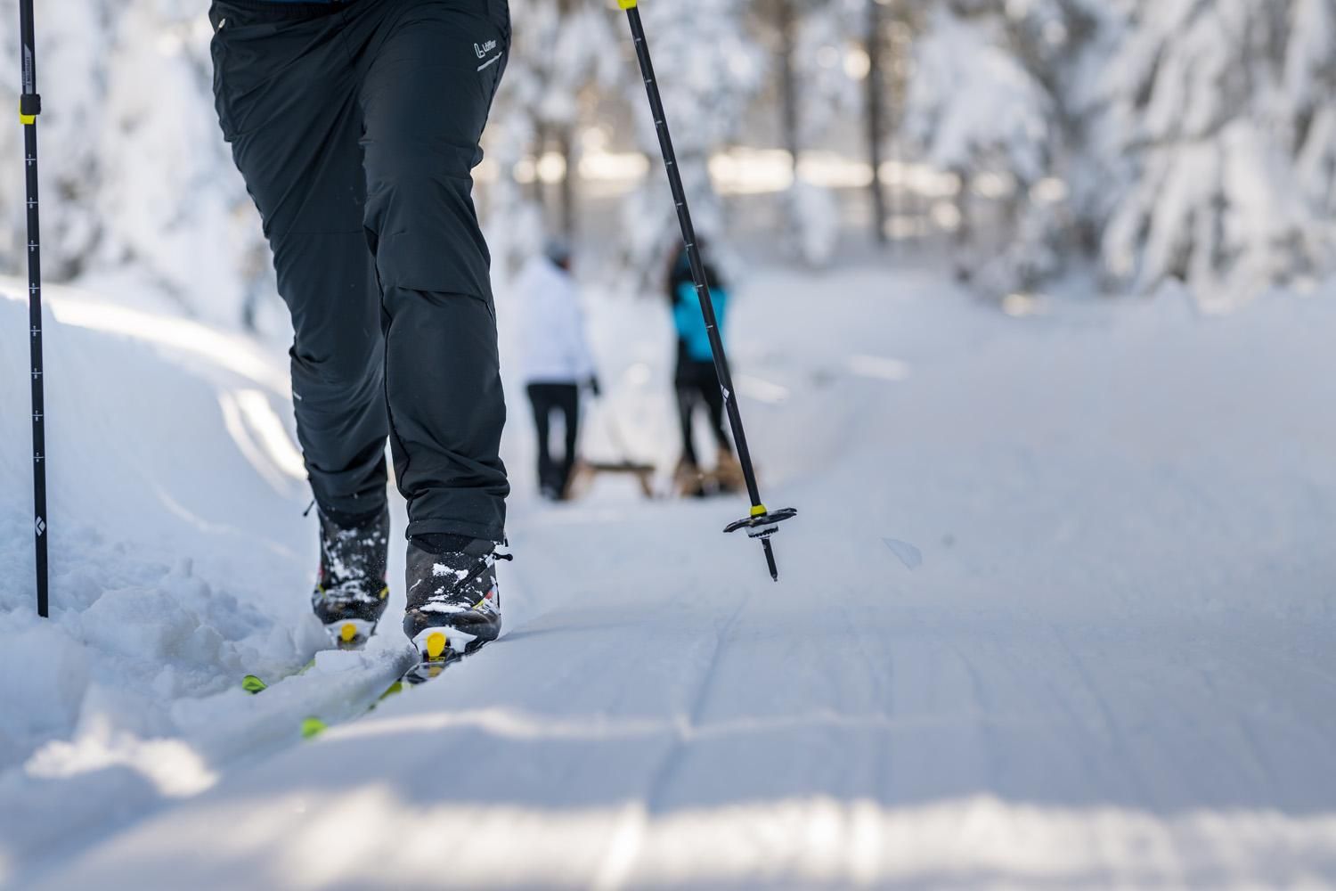 A skier is moving on a snow-covered track. In the background, other people can be seen in a winter setting.