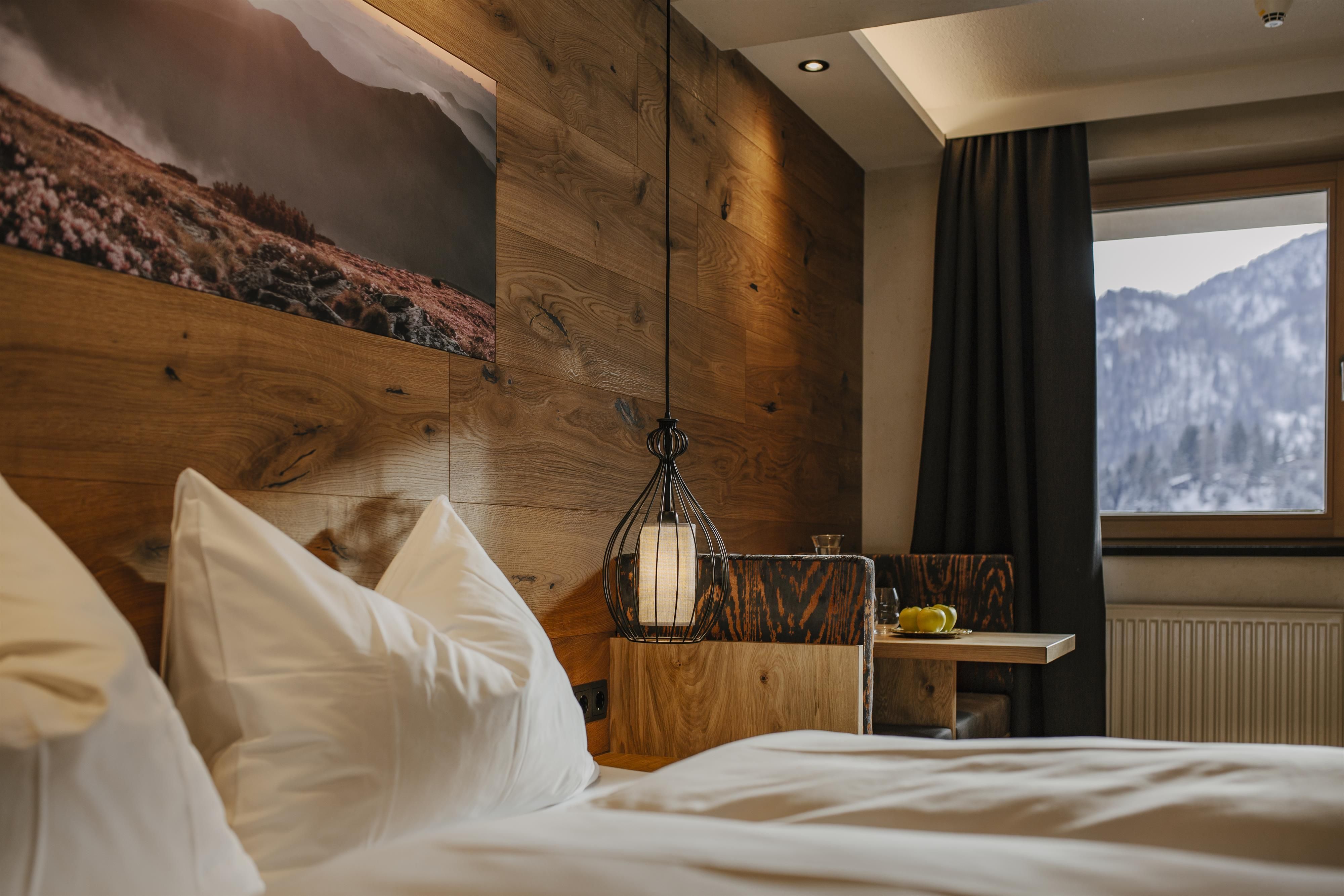 A cozy bedroom with wooden paneling and modern elements. The window offers a view of snow-covered mountains.