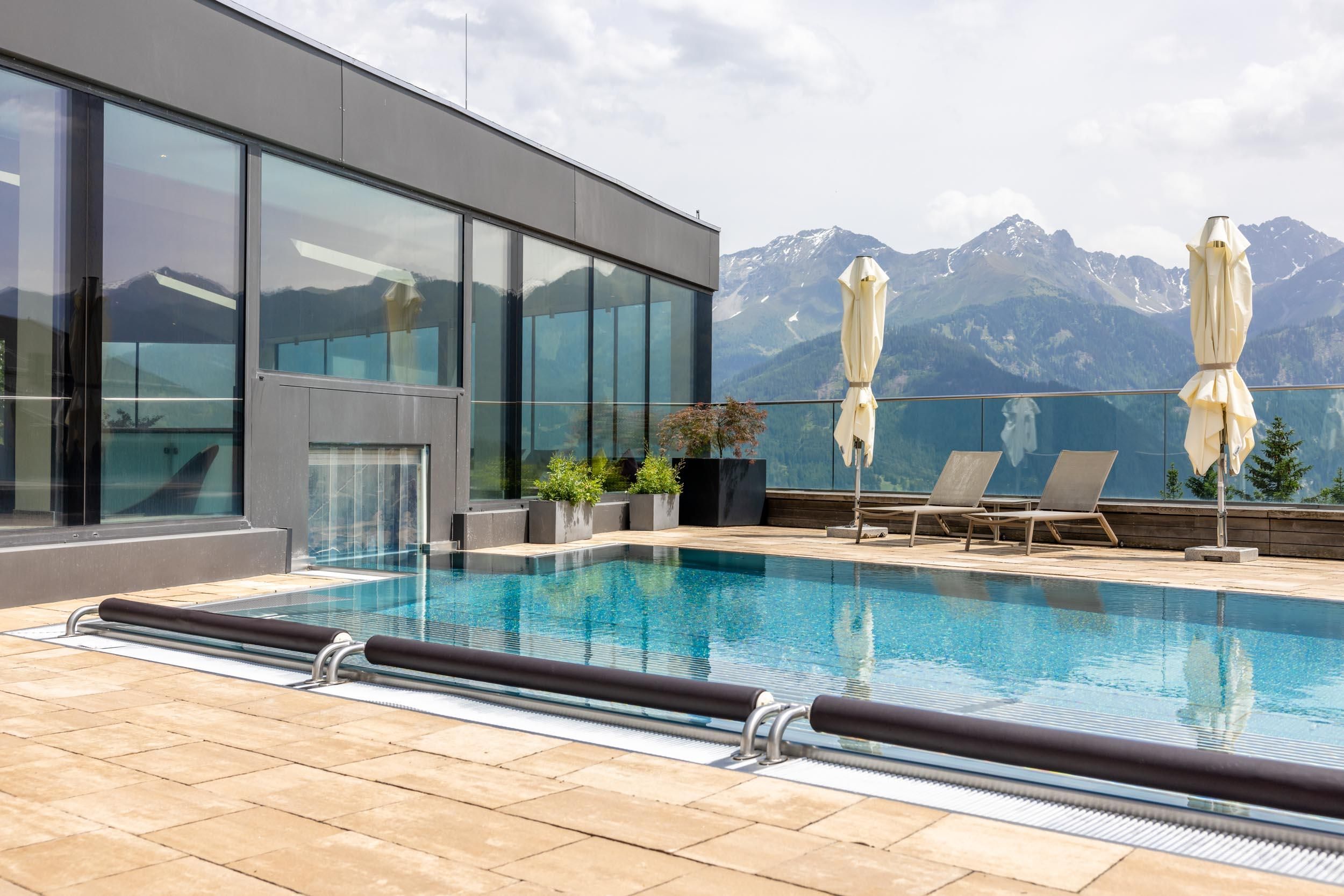 A modern panoramic outdoor pool with a view of the mountains. Umbrellas and loungers invite you to relax.