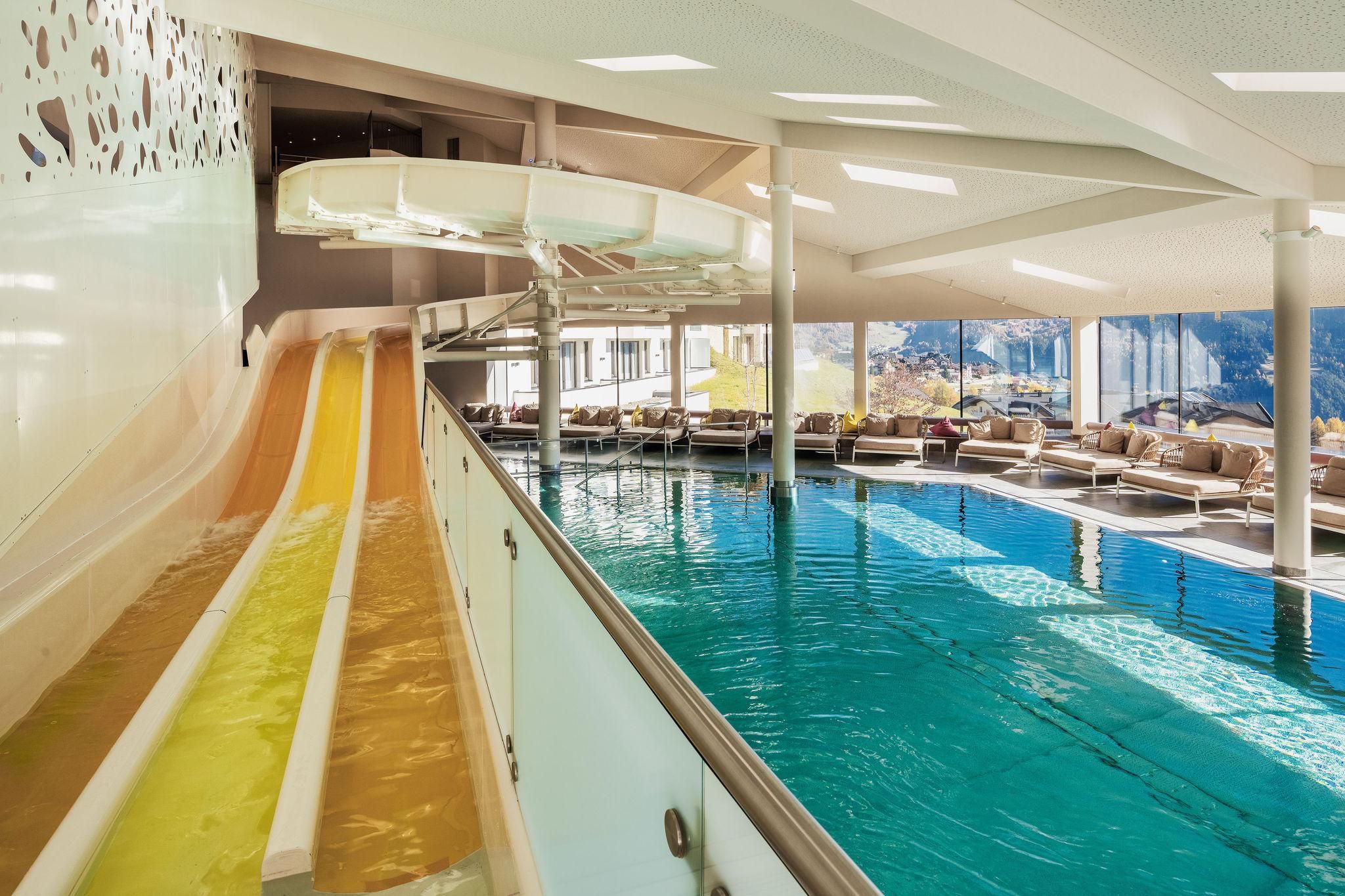 Family water world with indoor pool featuring a triple racing slide in bright colors. Cozy loungers are arranged around the pool.