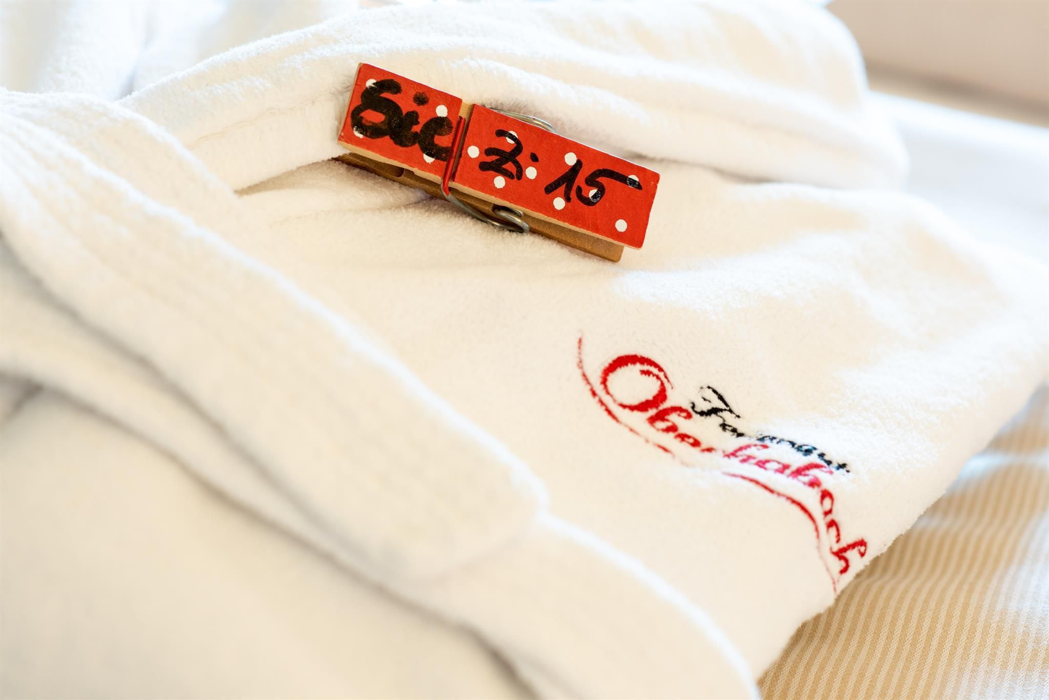 A white bathrobe is lying on the bed. A small clothespin with a number is attached to it.