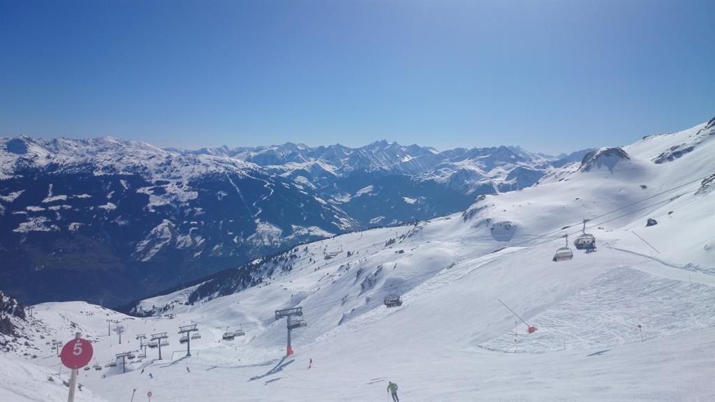A snowy mountain landscape with ski lifts and majestic mountains in the background. The sky is clear and sunny.