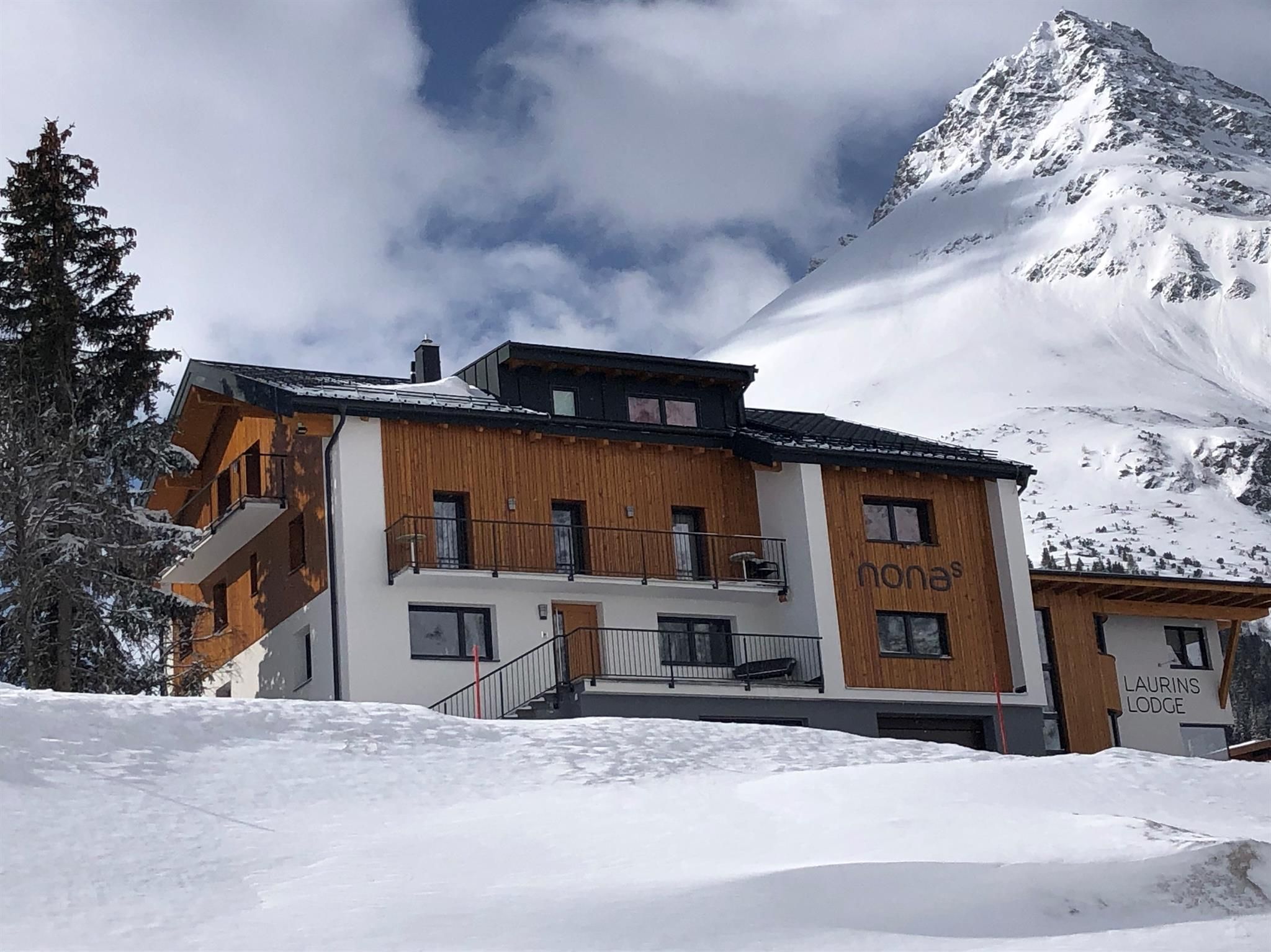 A charming mountain house in the snow, surrounded by tall mountains. The sky is cloudy, giving the scene a calm atmosphere.