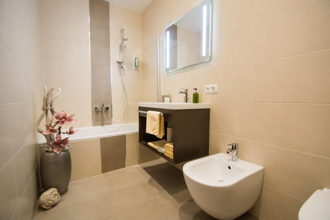 A modern bathroom with a bathtub, shower, and an elegant sink. The walls are kept bright, and decorative plants give the room a fresh touch.