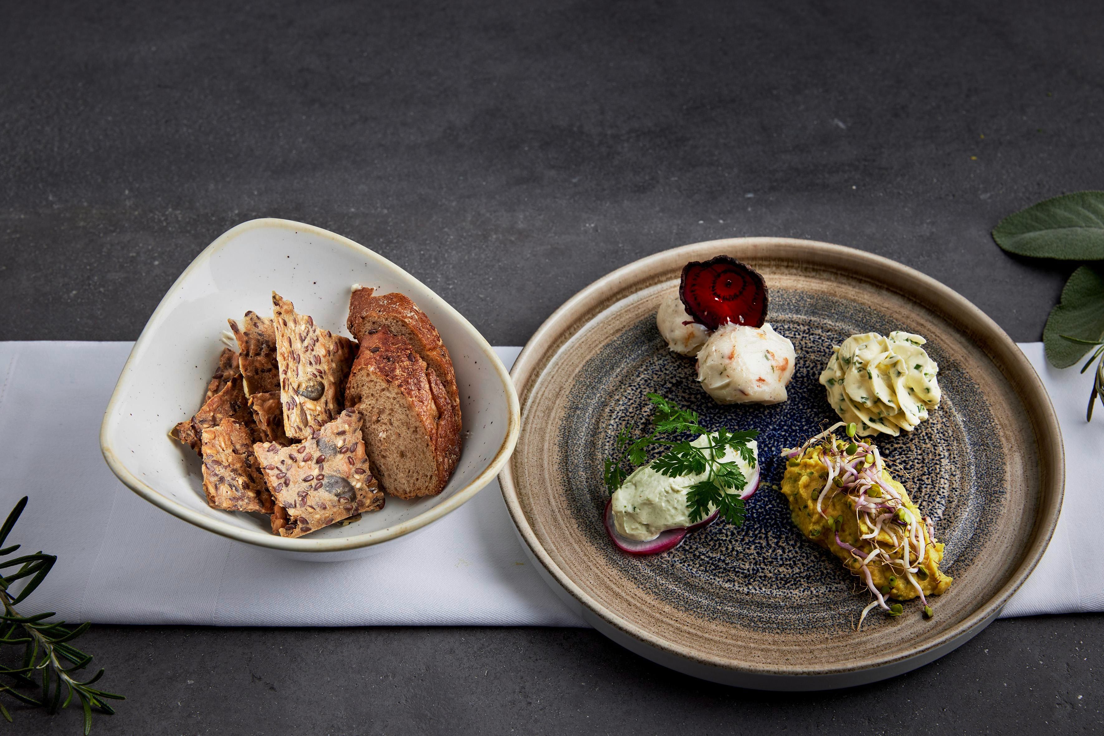 An attractively arranged platter with various appetizers such as vegetables and dips. Accompanied by crispy bread in a separate bowl.