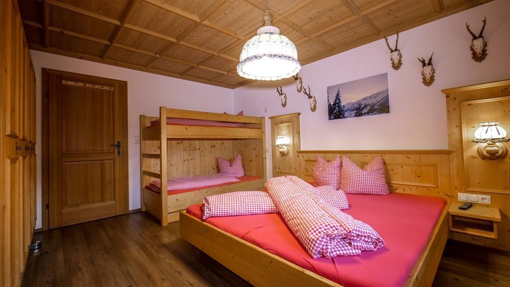 A cozy wooden bedroom with a double bed and a bunk bed. The atmosphere is warm and inviting, ideal for a relaxing stay.