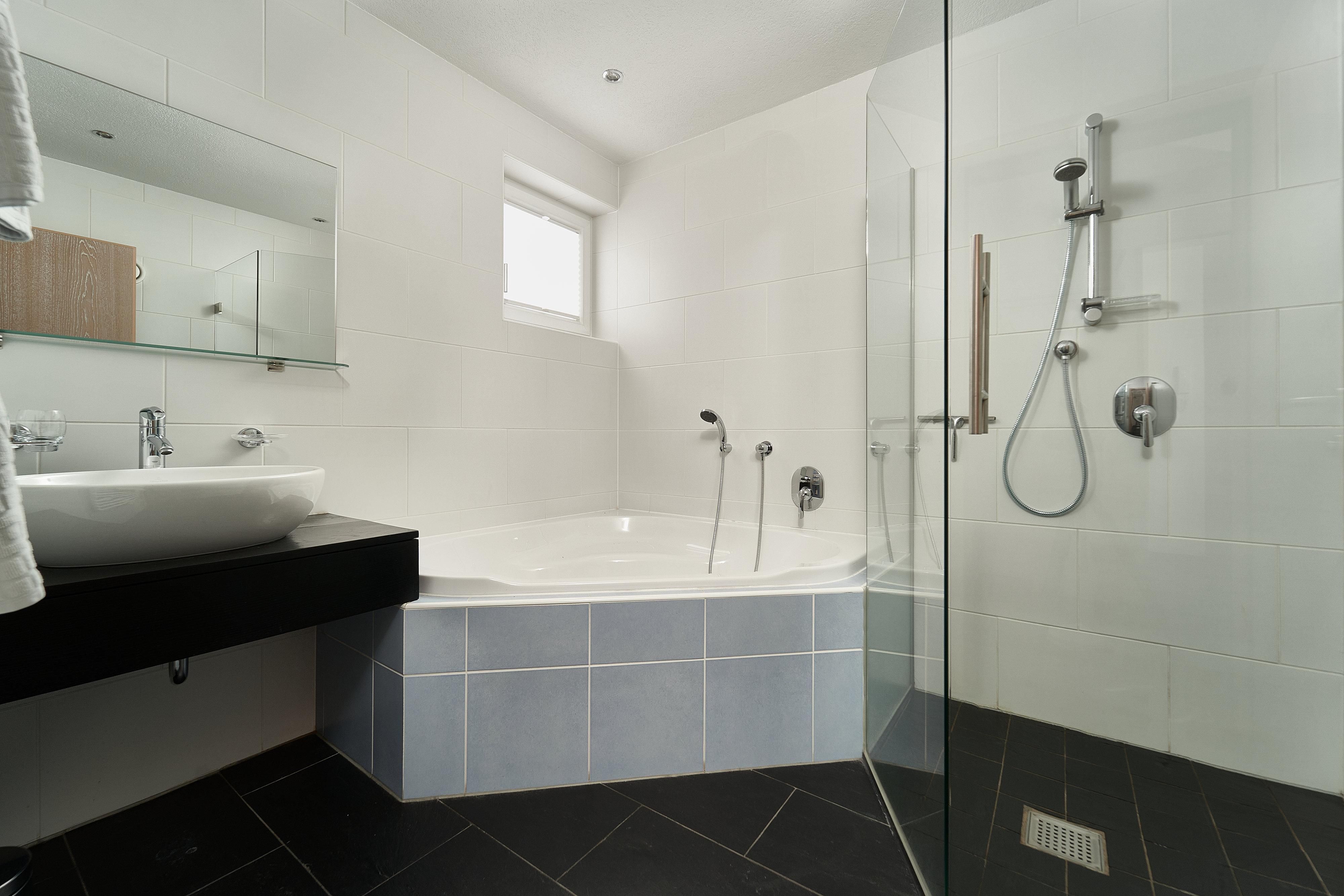 A modern bathroom with a shower and a bathtub. The walls are in neutral colors and the floor is dark.