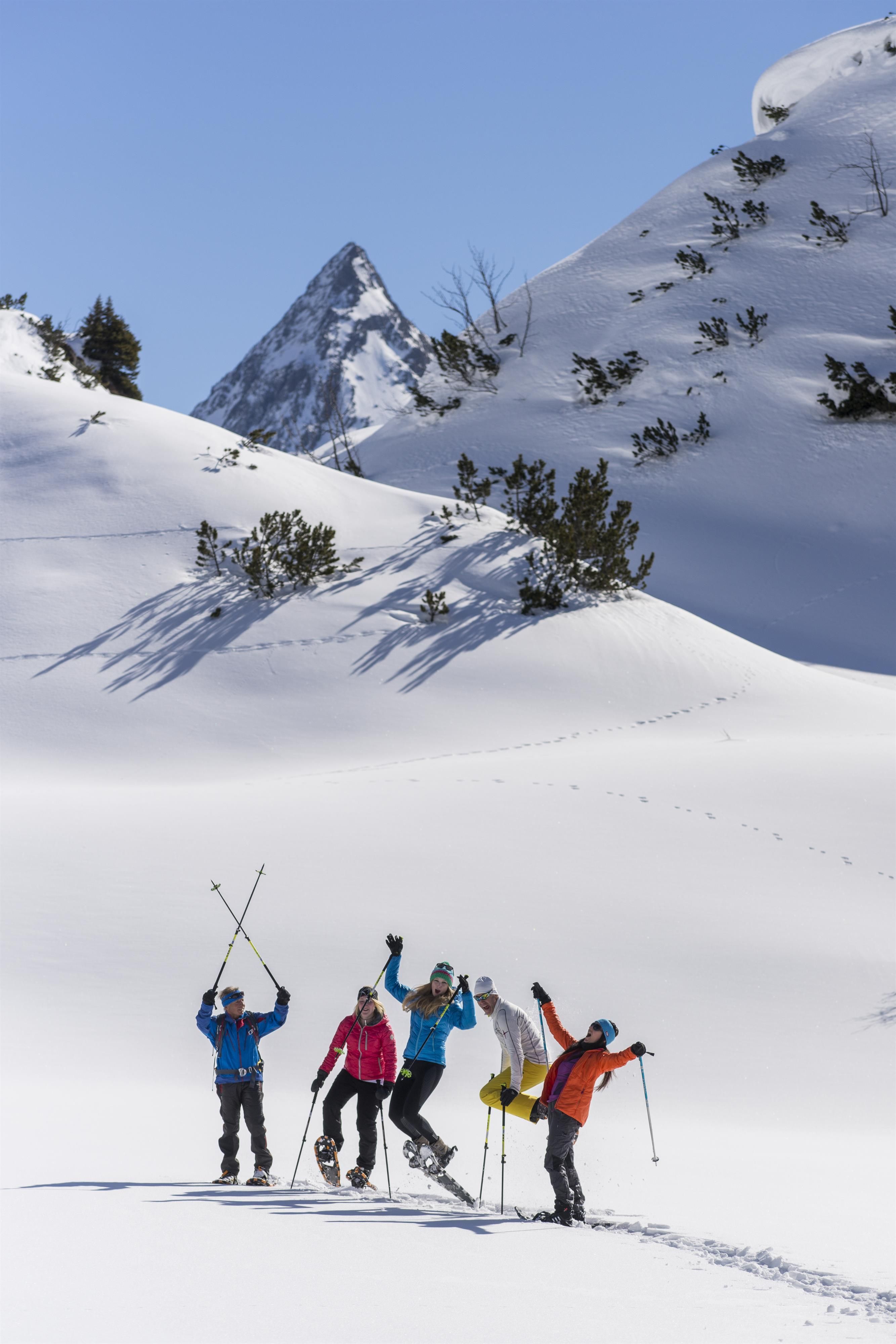 A group of four people is enjoying a sunny day in the snow. They are standing on a snowy slope and raising their arms in the air.