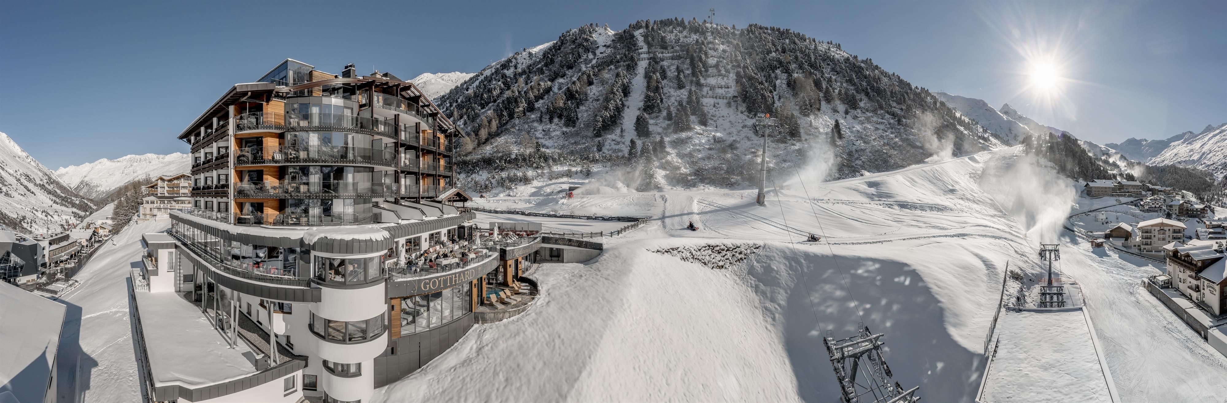 A modern hotel in a snowy ski resort. In the background, mountains and ski lifts are visible.