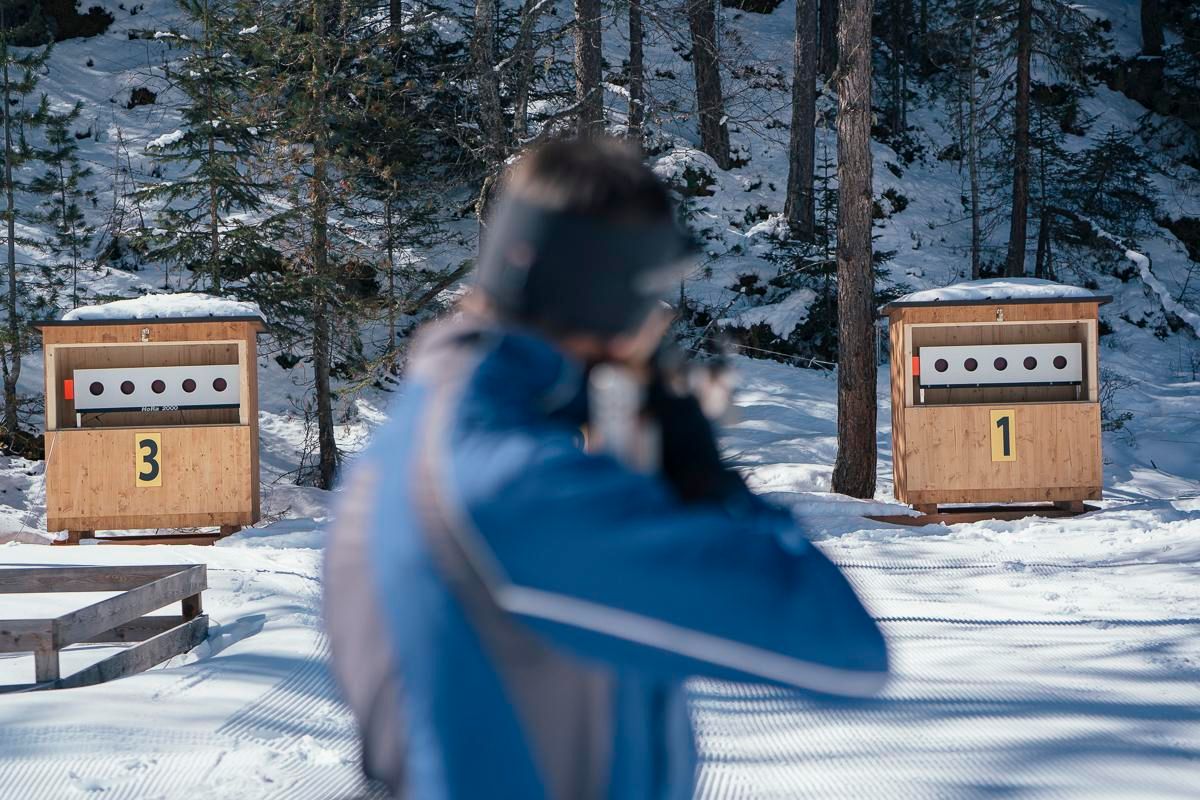 An archer aims at a target in nature. In the background, the target huts numbered 1 and 3 can be seen.