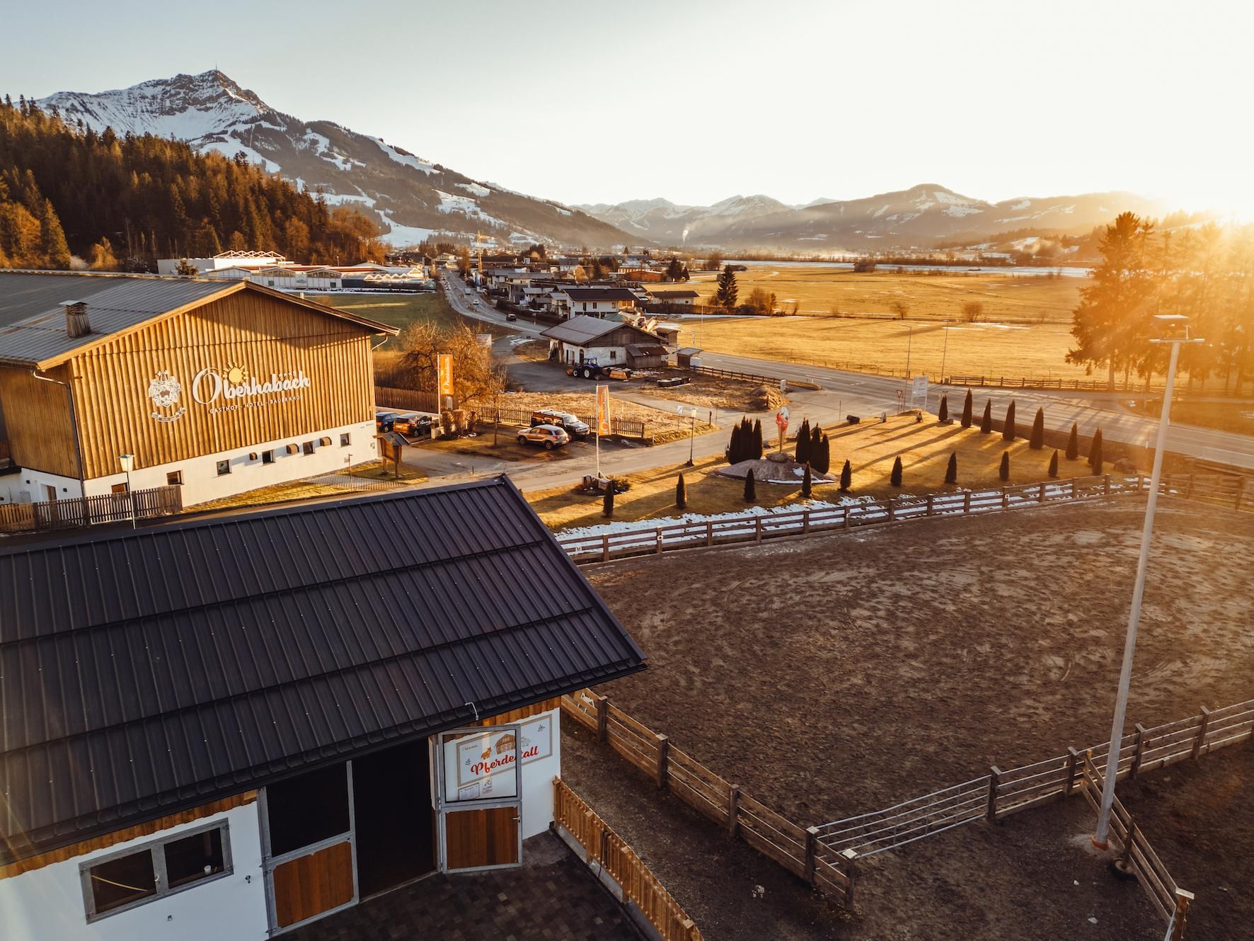 A picturesque landscape with a traditional wooden house and gentle hills in the background. The sun is shining, bathing the scene in warm light.
