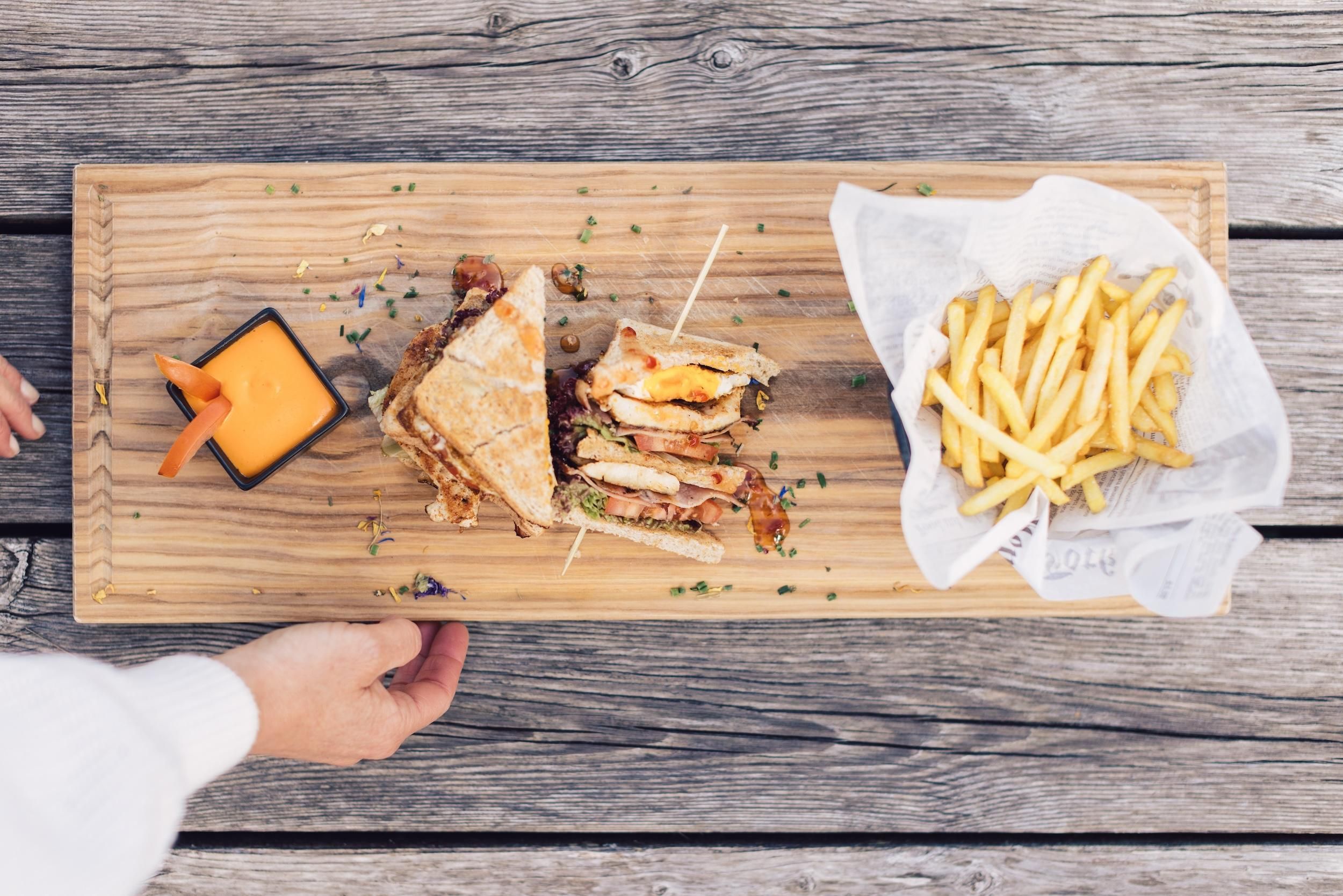 A wooden board with a sandwich, fries, and a dip sauce. The dish is attractively arranged and looks delicious.