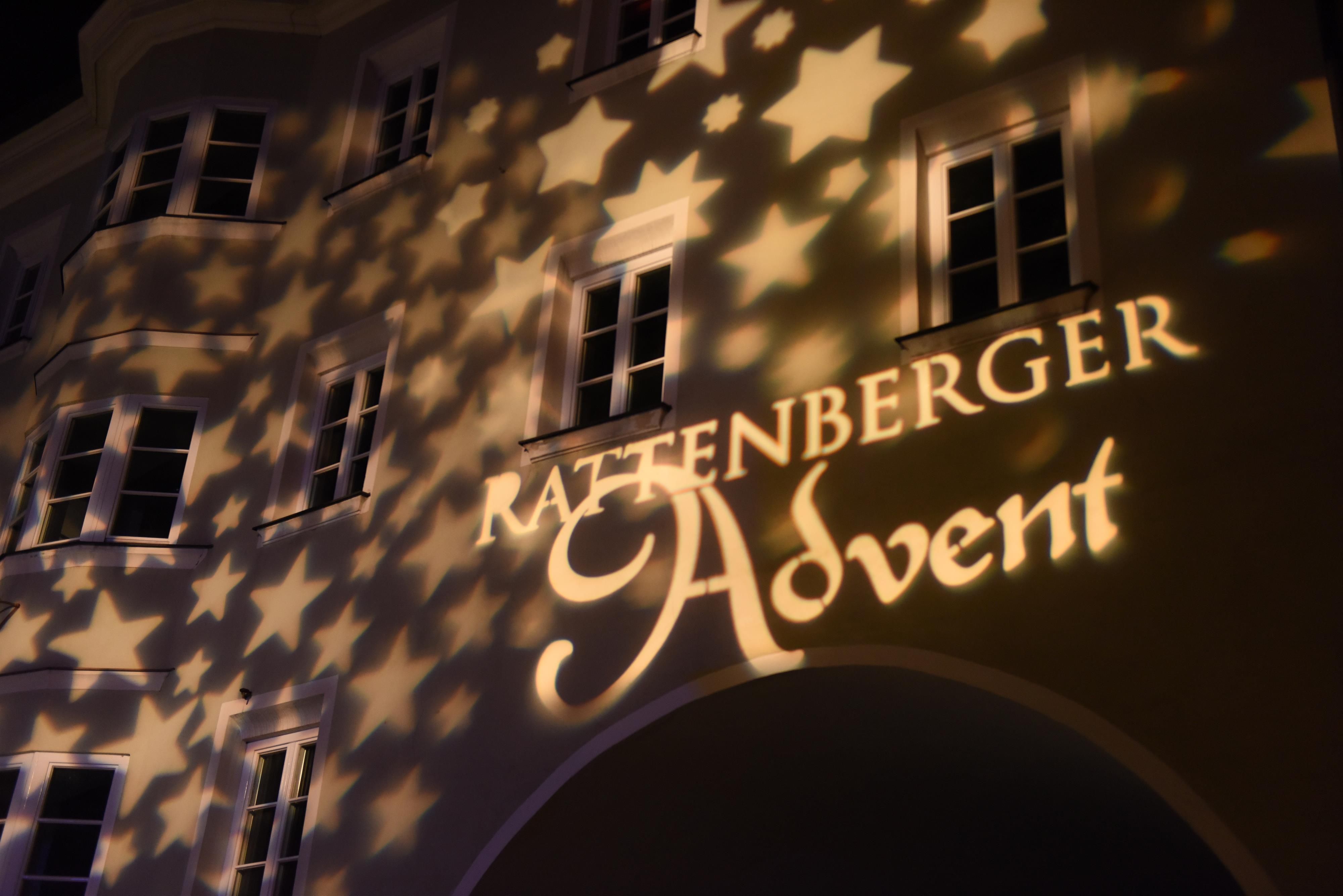 A building wall with the projected inscription "Rattenberger Advent" and a pattern of glowing stars. The lighting creates a festive atmosphere.
