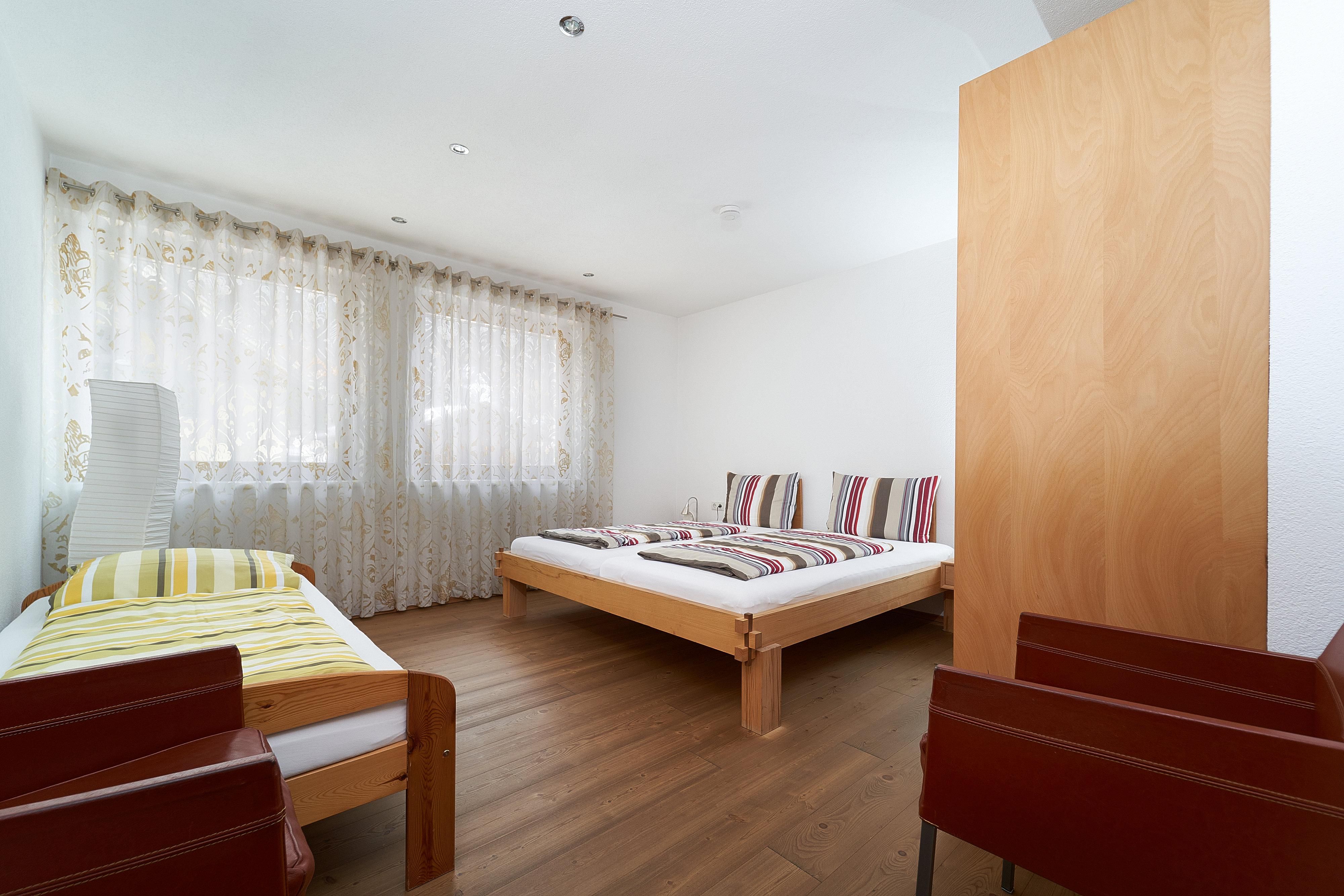 A simple room with two beds and an additional bed. The walls are light, and the light through the curtains is friendly.