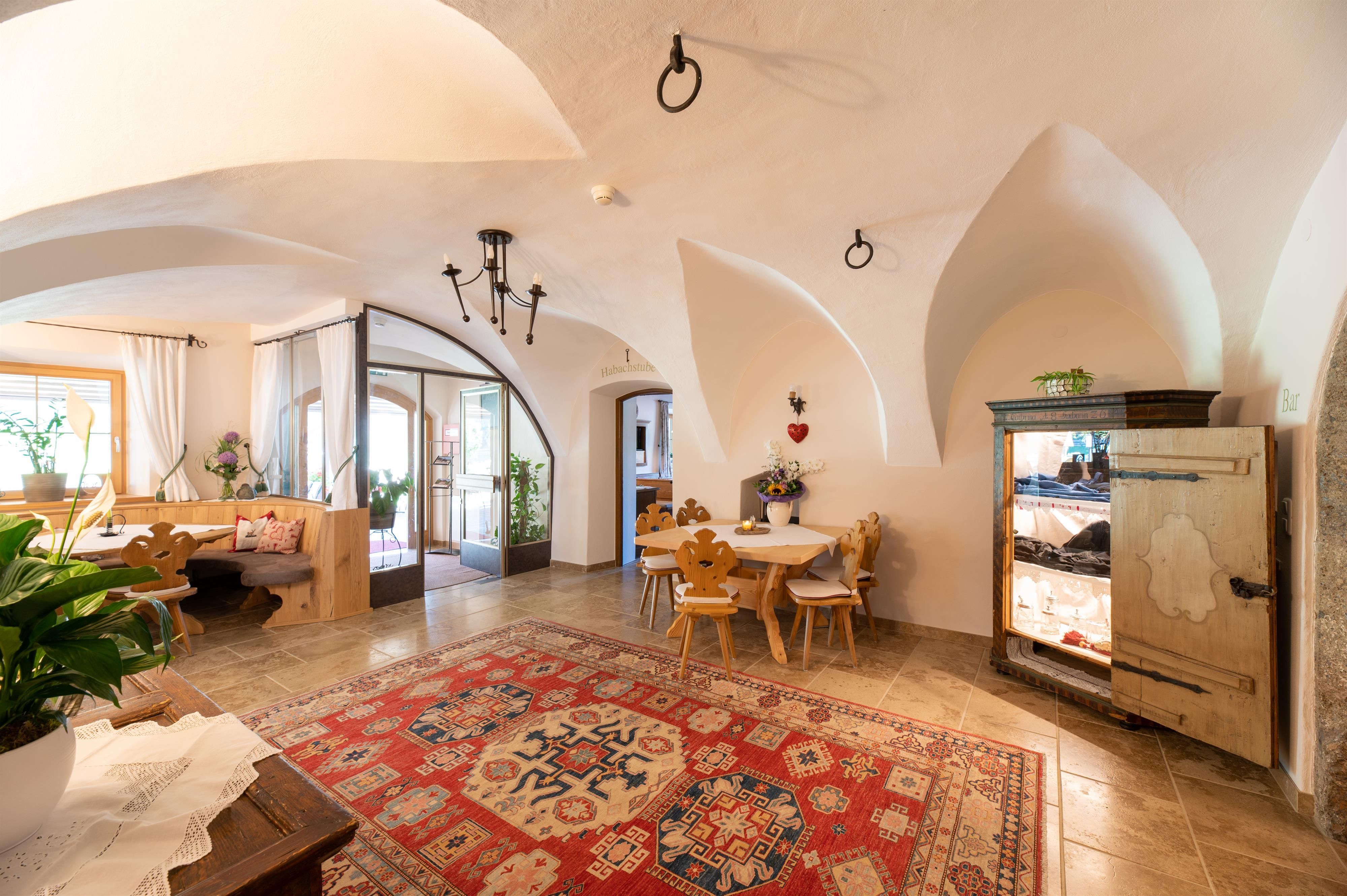 A cozy room with a large rug, dining tables, and chairs. It is warm and welcoming, with beautiful architectural details.