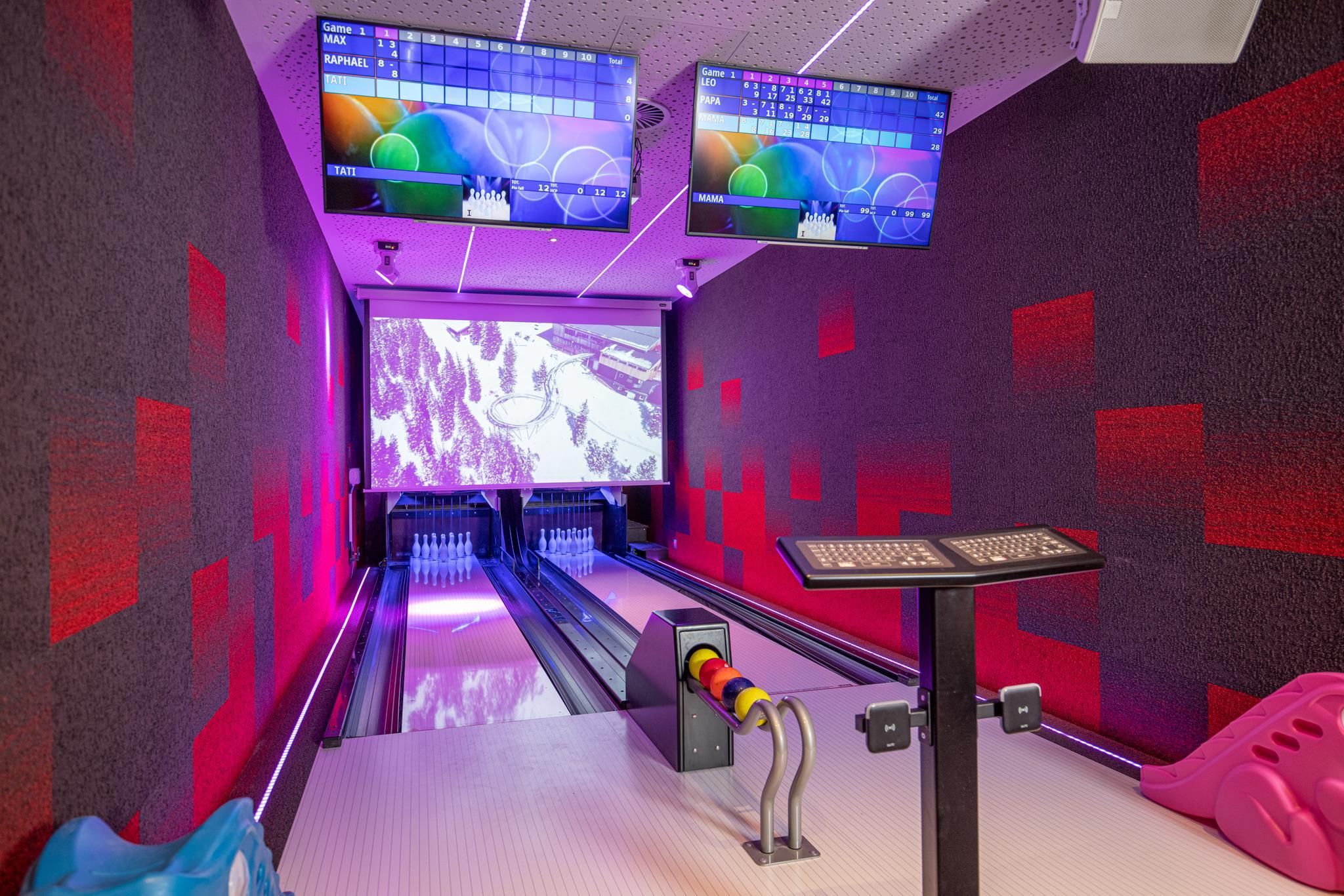 A modern bowling area with colorful walls and two large screens. The lane is well-lit and ready for fun and entertainment.