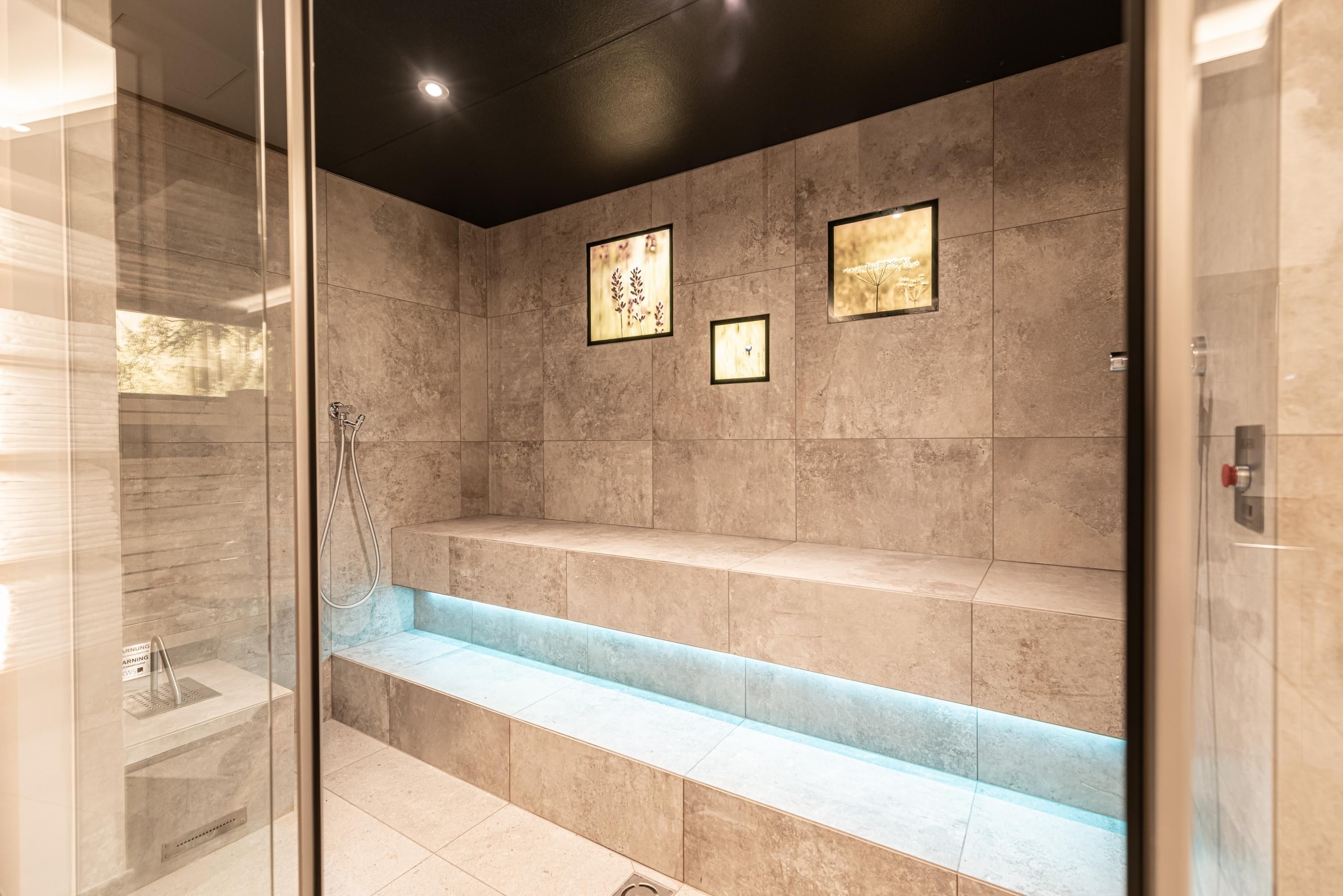 An elegant steam bath with bright tiles and indirect lighting. Decorative pictures are hanging on the walls.