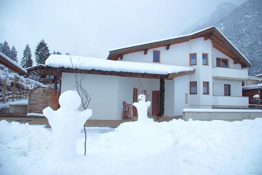 A modern house in the snow with snow-covered trees. In the foreground, there are two snowmen.