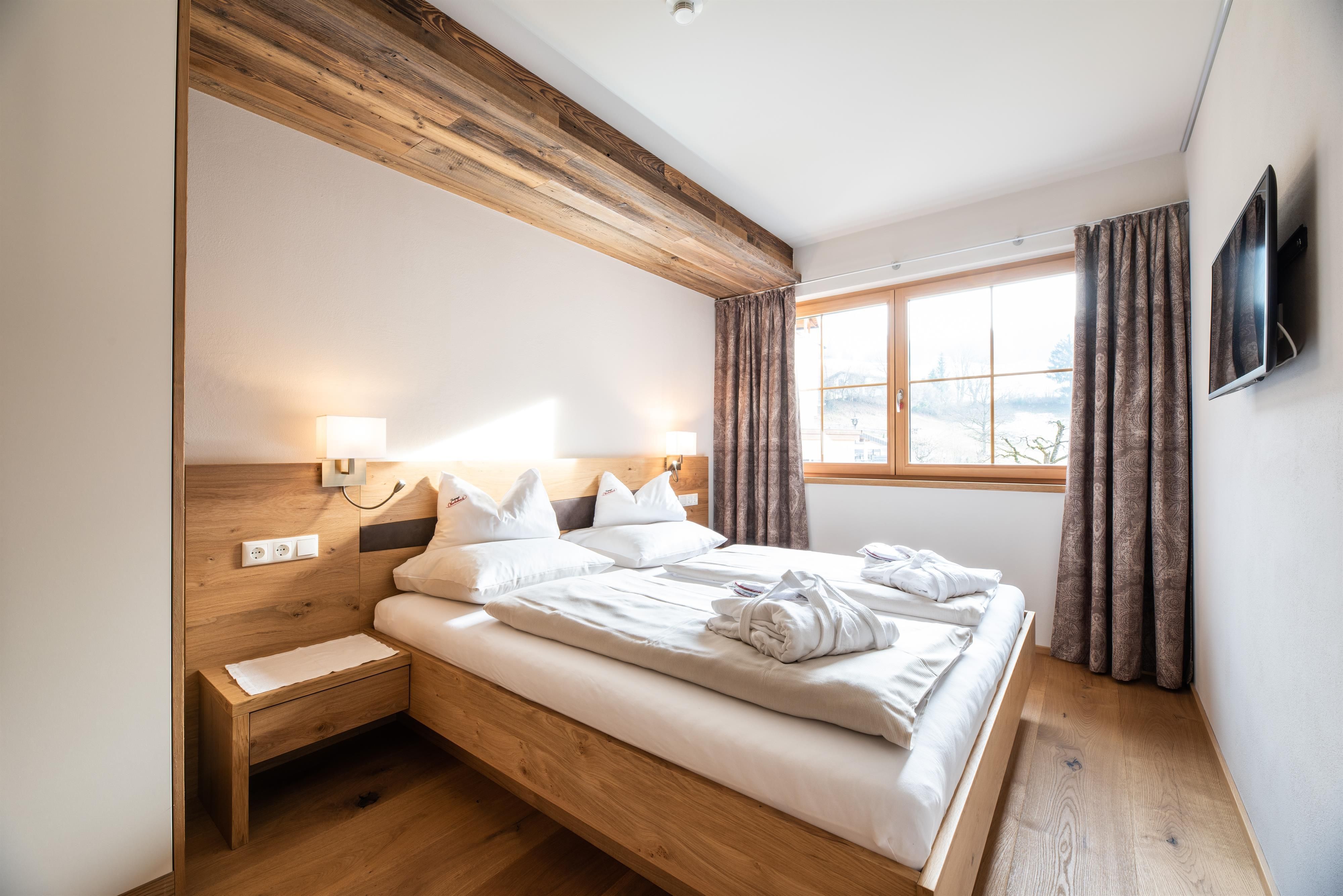 A cozy bedroom with a wooden double bed and modern amenities. The room has large windows that provide plenty of daylight.