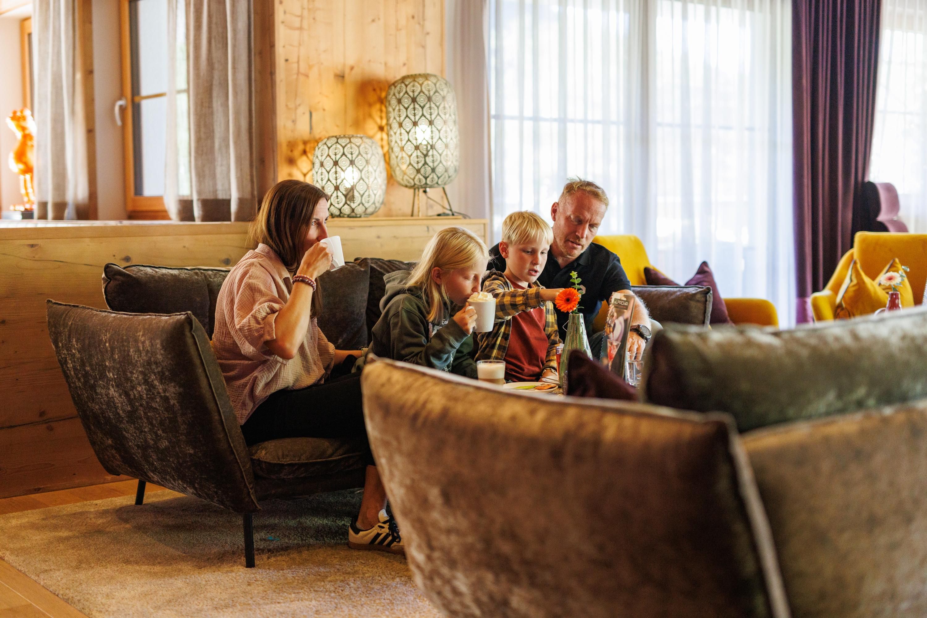 A family sits comfortably in a modern living room. They are enjoying drinks and spending time together.