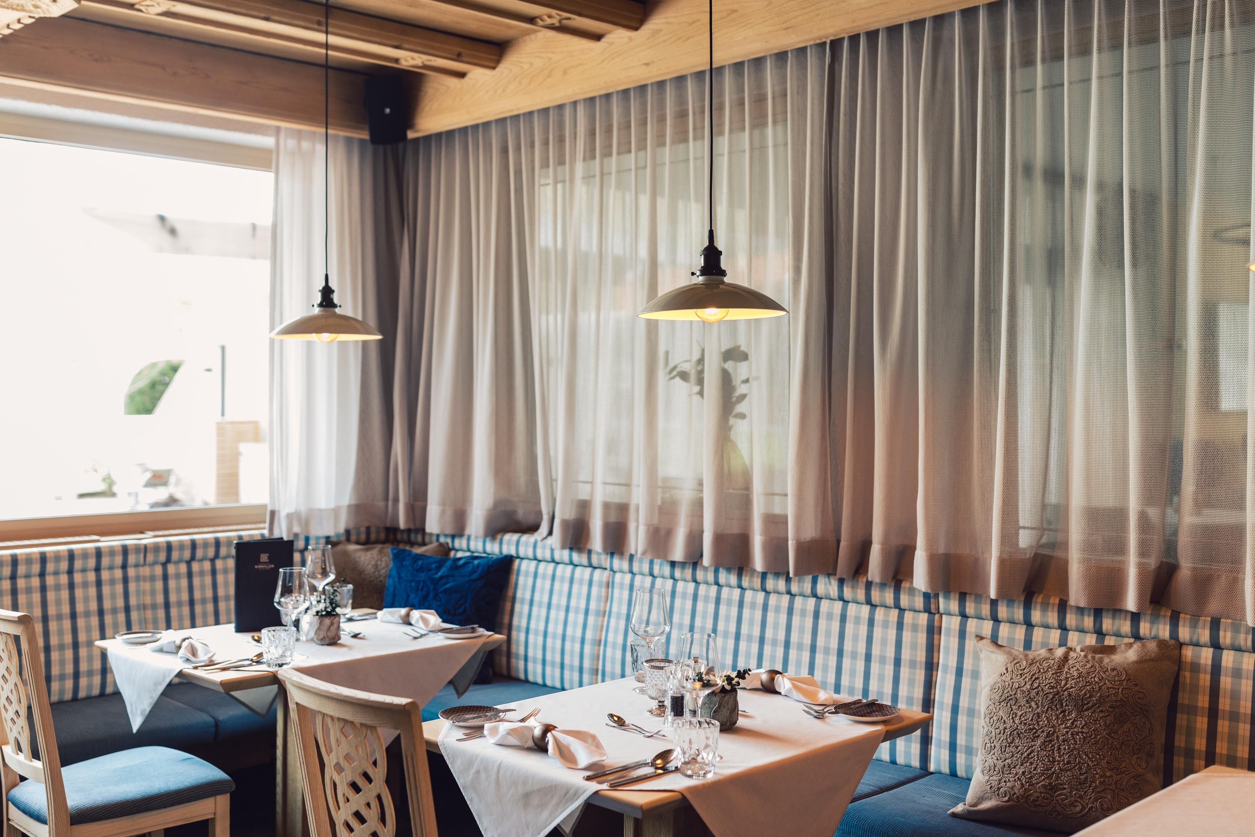 A cozy restaurant with bright windows and modern lamps. The tables are stylishly set with space for multiple guests.