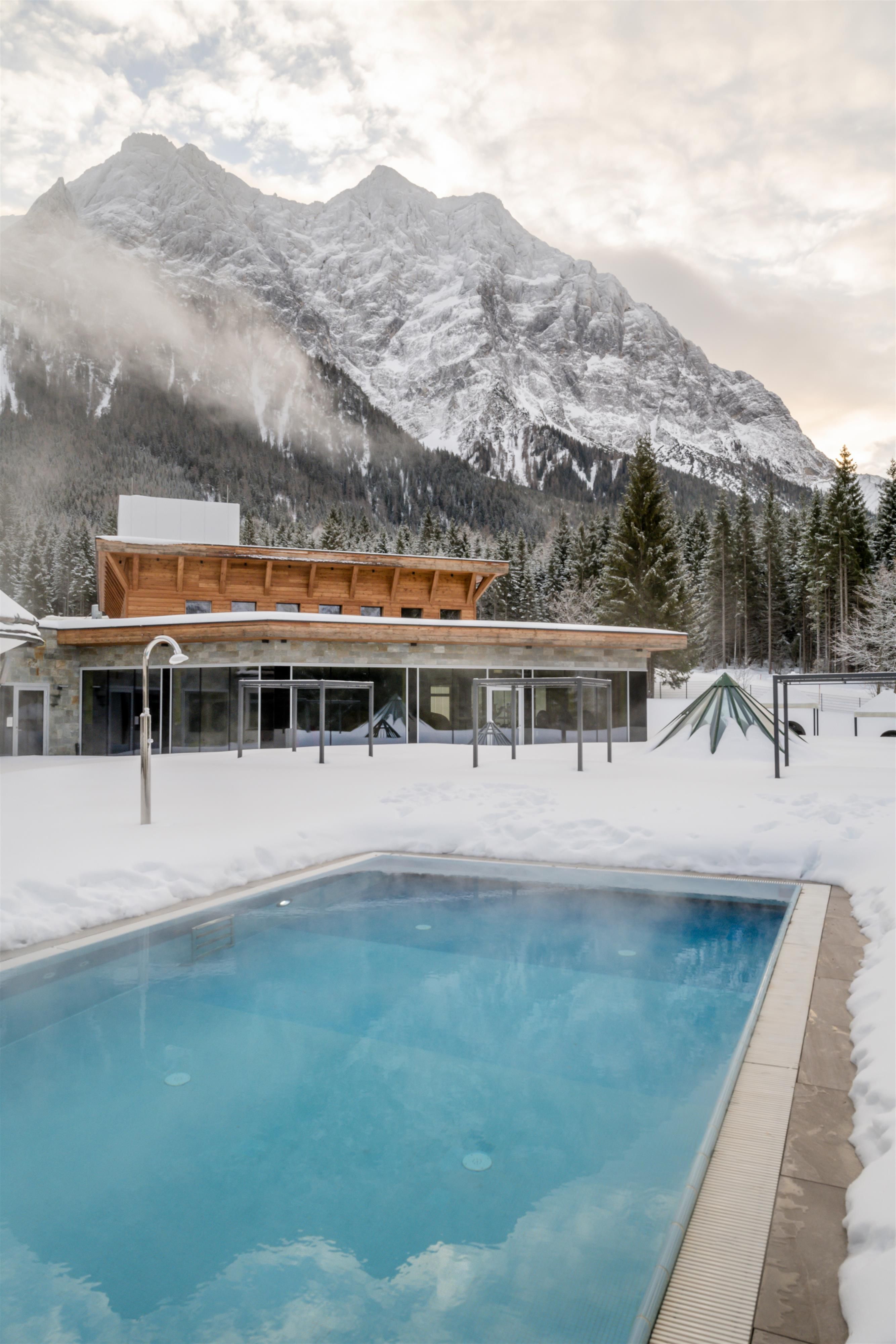A modern swimming pool in a snow-covered landscape, surrounded by majestic mountains. The atmosphere is calm and inviting.