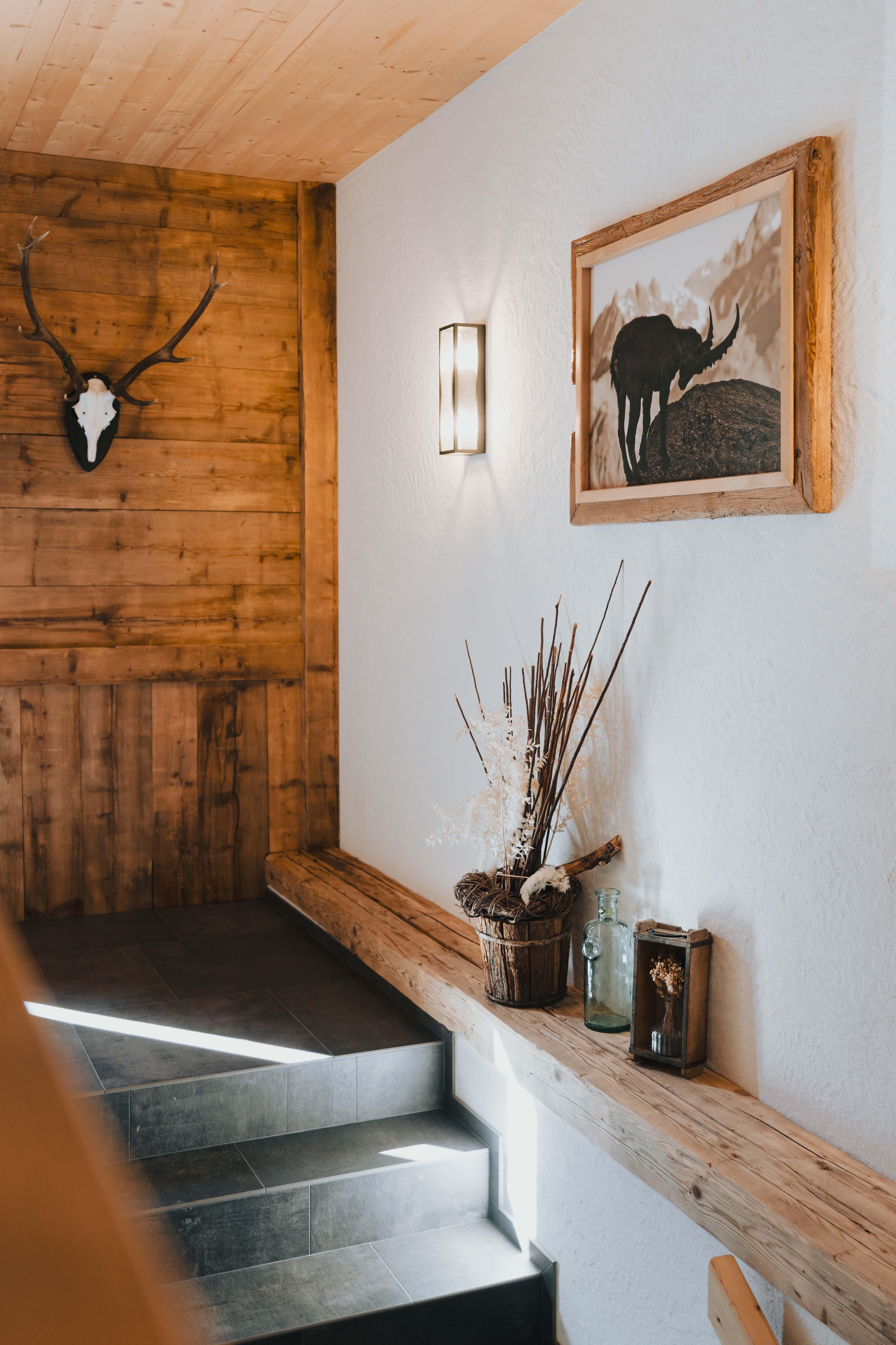 An inviting hallway with wooden walls and a painting of an animal. On the windowsill are decorative elements like dried flowers and glasses.