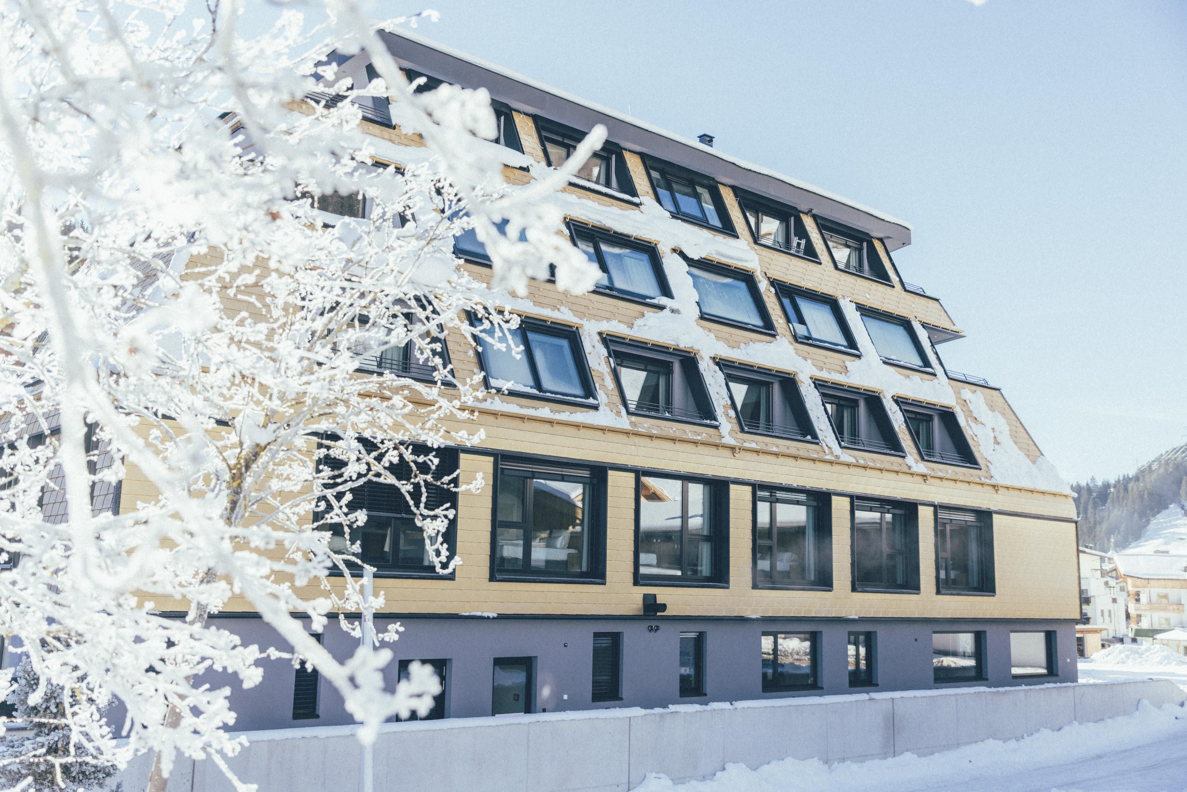 A modern building in winter, surrounded by snow. The windows reflect the clear blue of the sky.