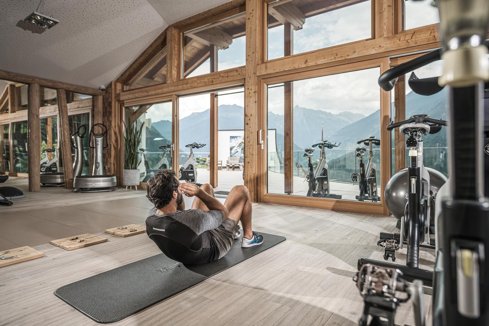 A modern gym with large windows and a view of the mountains. A person is doing abdominal exercises on a mat.