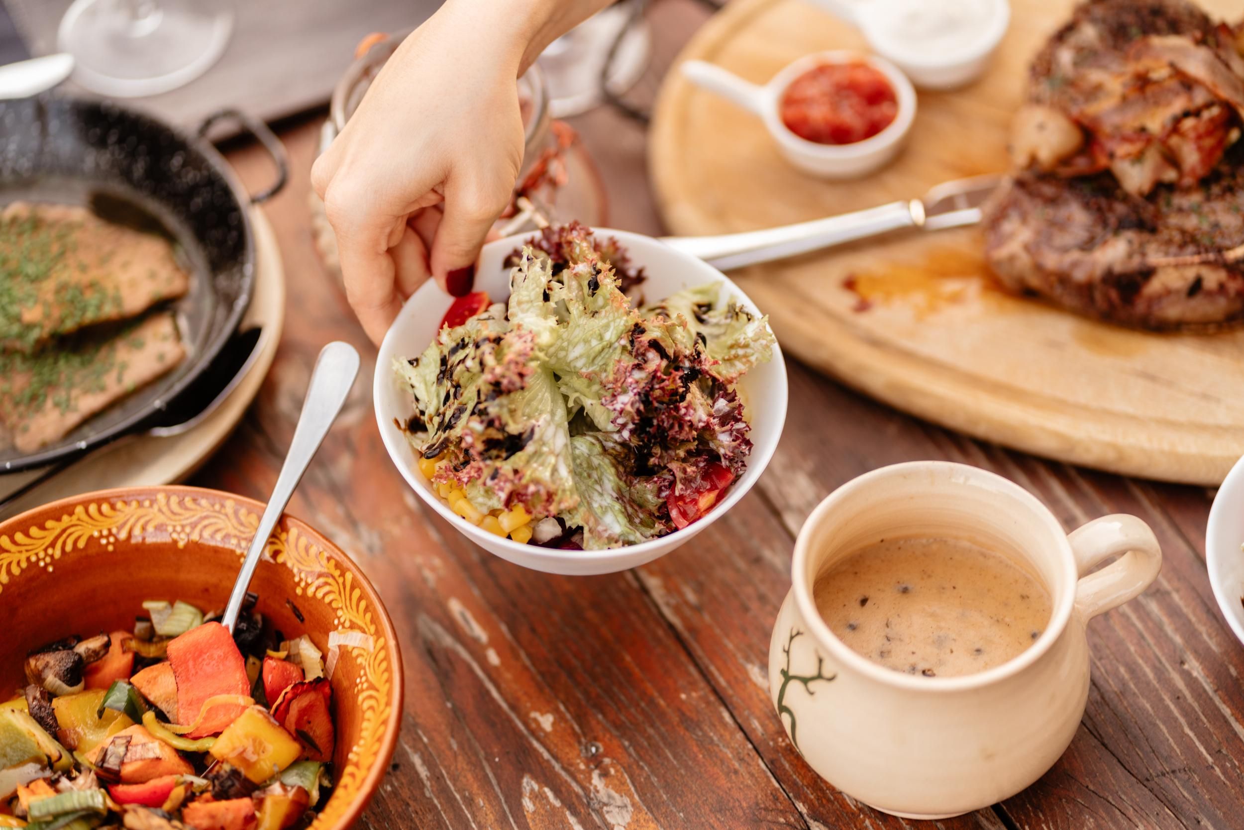 A table with various dishes, including a colorful salad and a bowl of vegetables. In the background, there are also meat dishes and a drink visible.