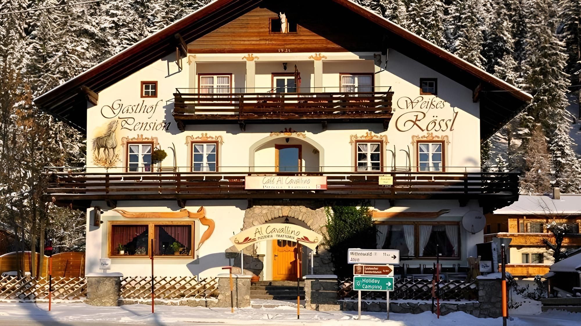 A cozy house in the snow with wooden decorations and balconies. Surrounded by snow-covered trees, it emanates an inviting atmosphere.
