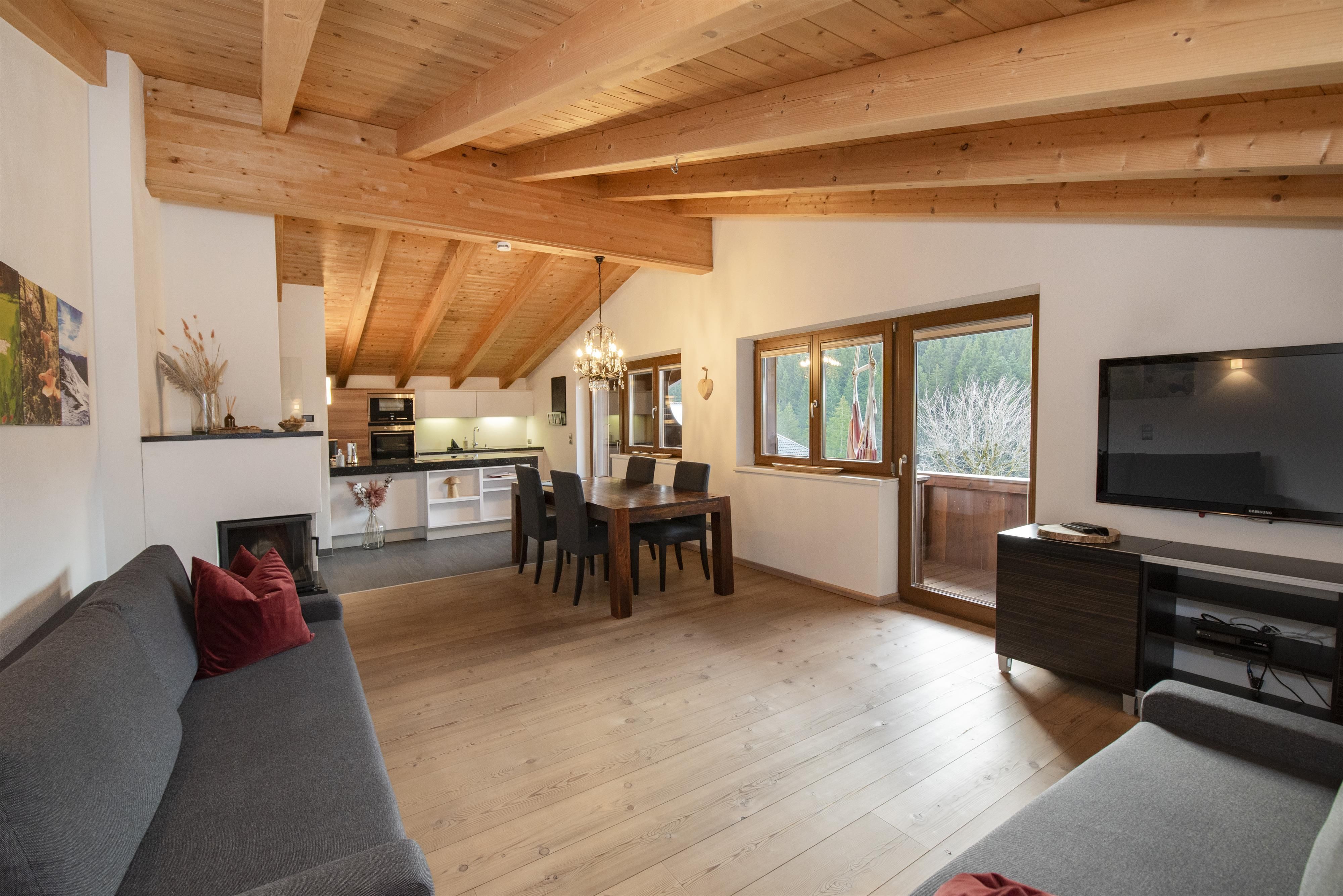 A cozy living space with a wooden ceiling and modern furniture. The large window front provides plenty of daylight and a view of the outdoors.