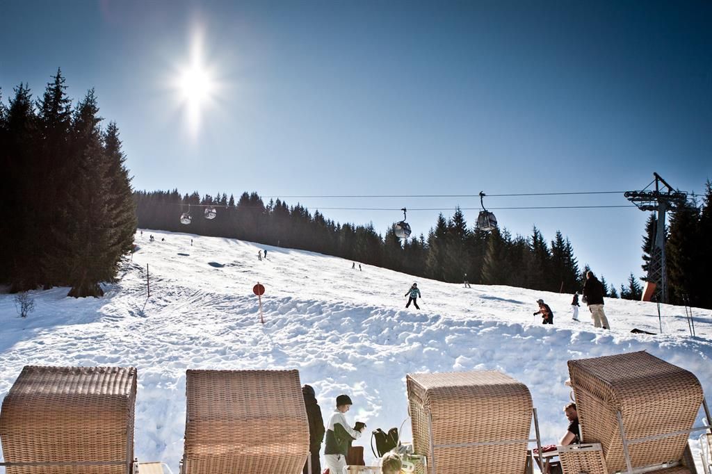 A sunny day on the slopes in the mountains with snow-covered pistes. In the foreground are comfortable lounge chairs, while skiers descend the slope.