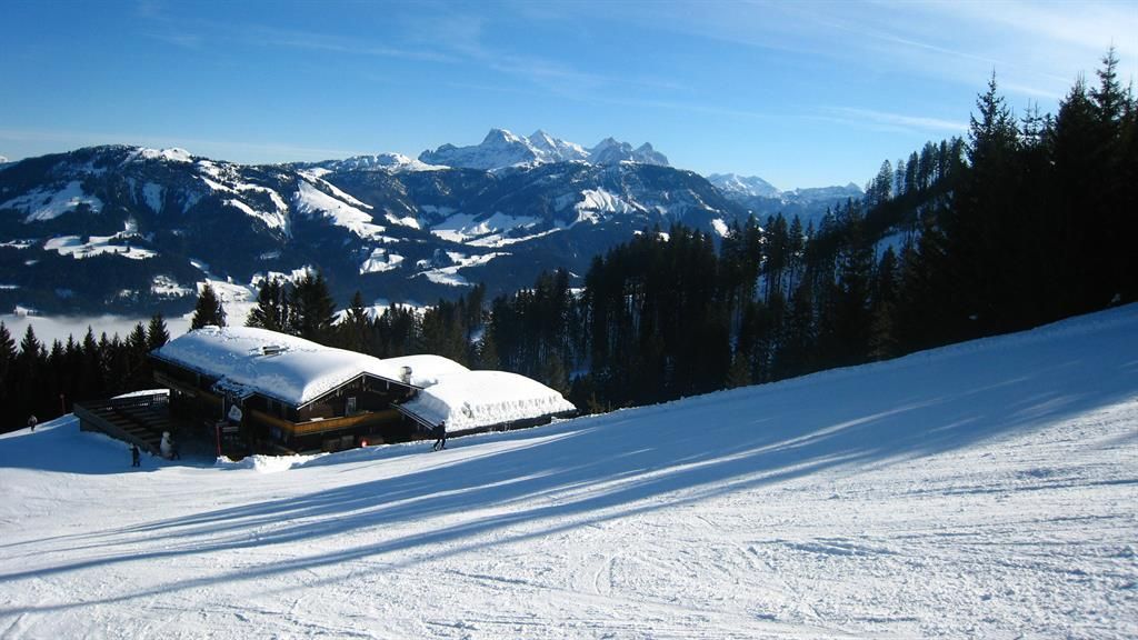 A picturesque winter landscape with snow-covered mountains and a cozy chalet. The clear blue sky creates a relaxed atmosphere.