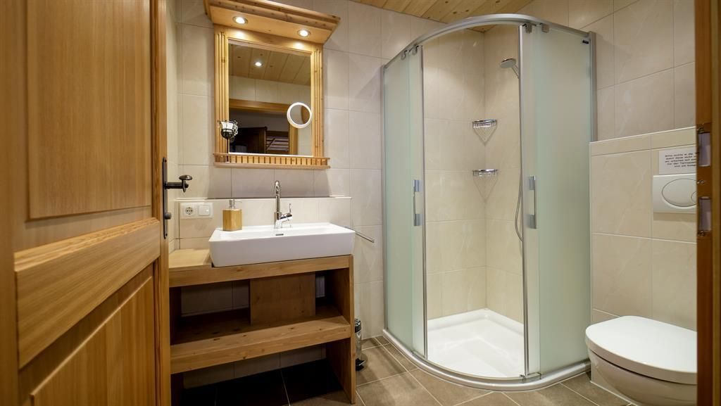 A modern bathroom with a shower and a large mirror. The walls are light and the wooden furniture creates a warm atmosphere.