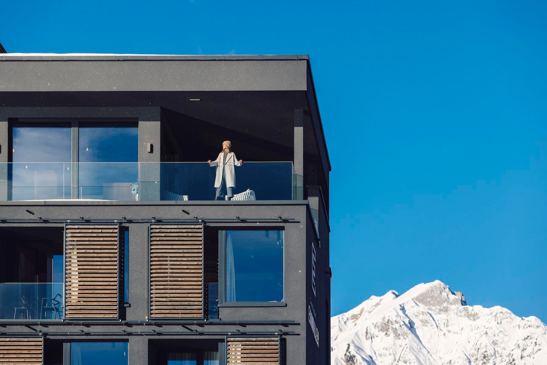 A modern apartment with a view of the mountains. A person is standing on the balcony and enjoying the view.