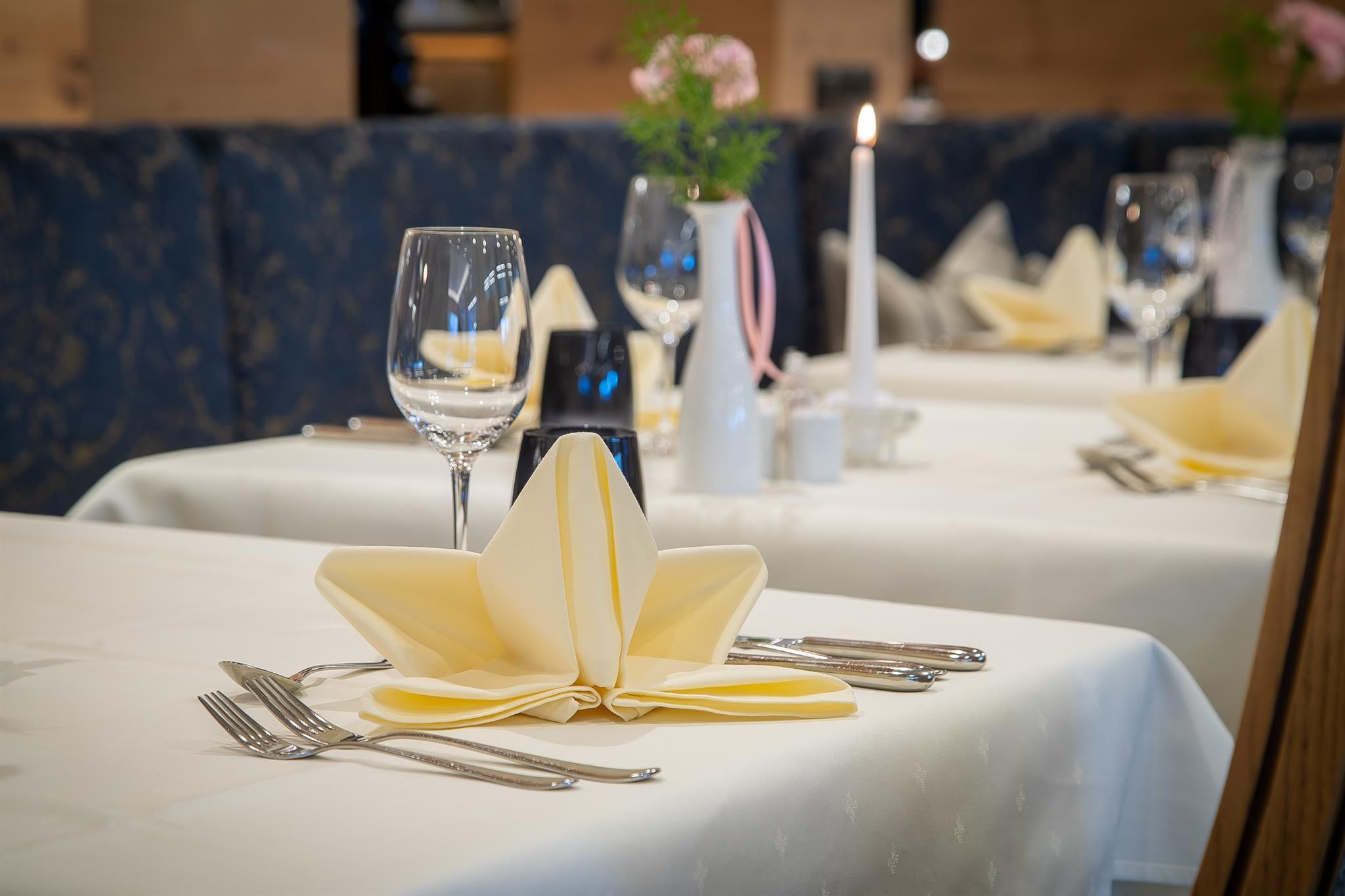 An elegant table with yellow napkins and glasses. In the background, decorative flowers and a candle are visible.